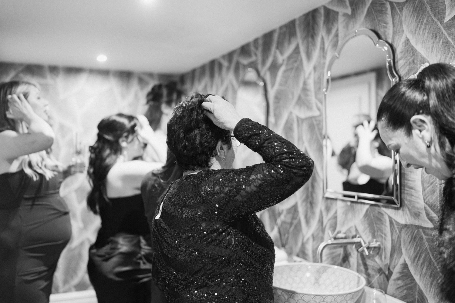 Guests fix hair and socialize in stylish bathroom with textured walls at wedding reception party.