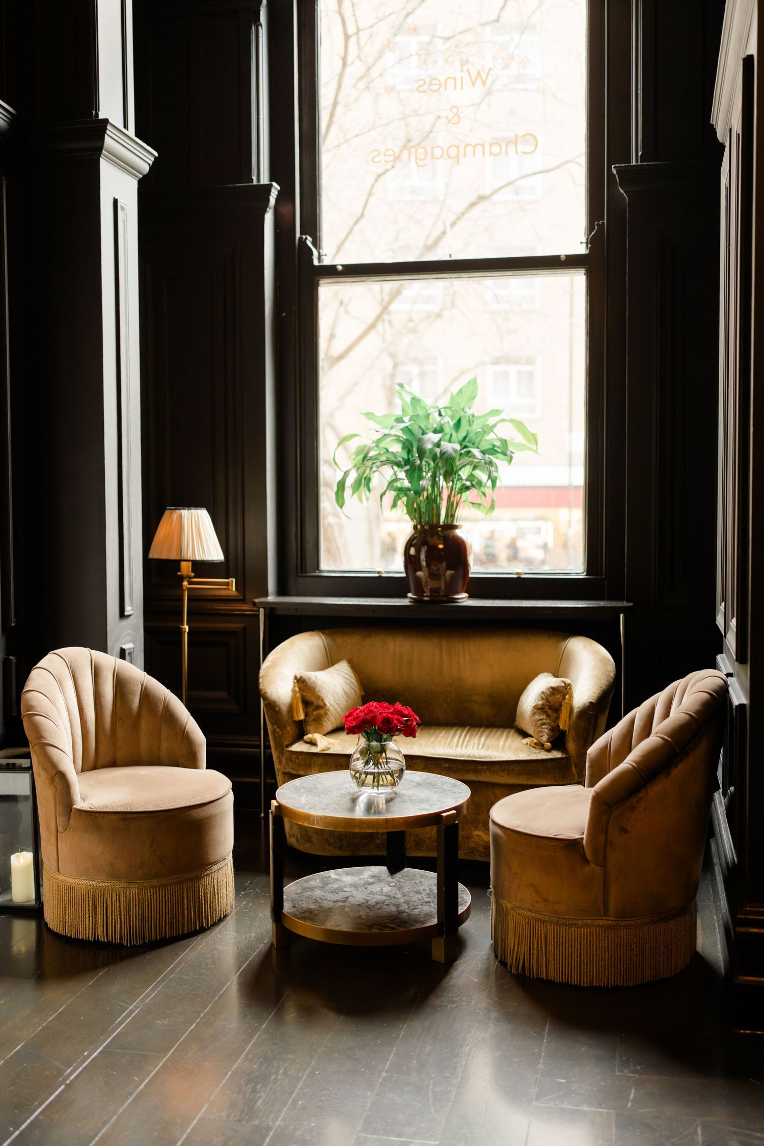 Elegant dark-walled lounge with gold velvet chairs, a sofa, and red roses on a marble table.