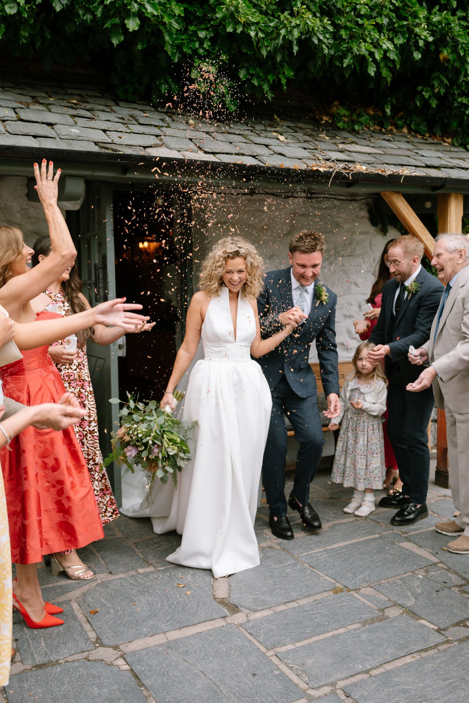 Wedding guests throw confetti during a joyful outdoor celebration on a stone patio.