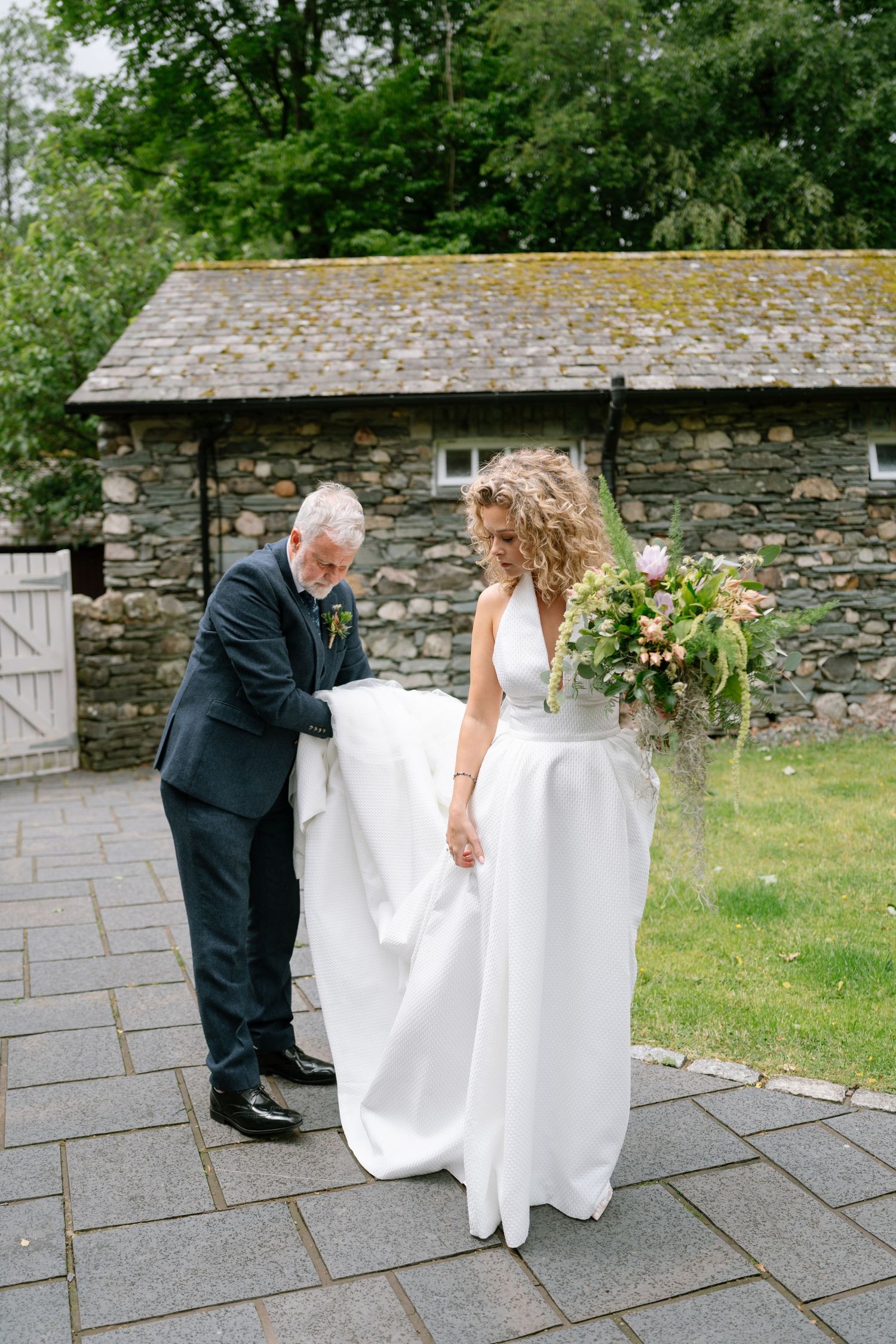 Wedding dress being adjusted outdoors against a rustic stone wall background.