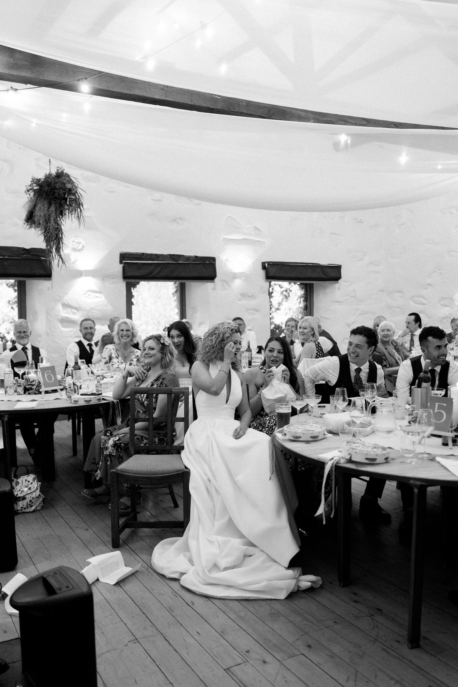 Black and white reception photo showing wedding celebrations in a rustic venue with white draped ceiling.