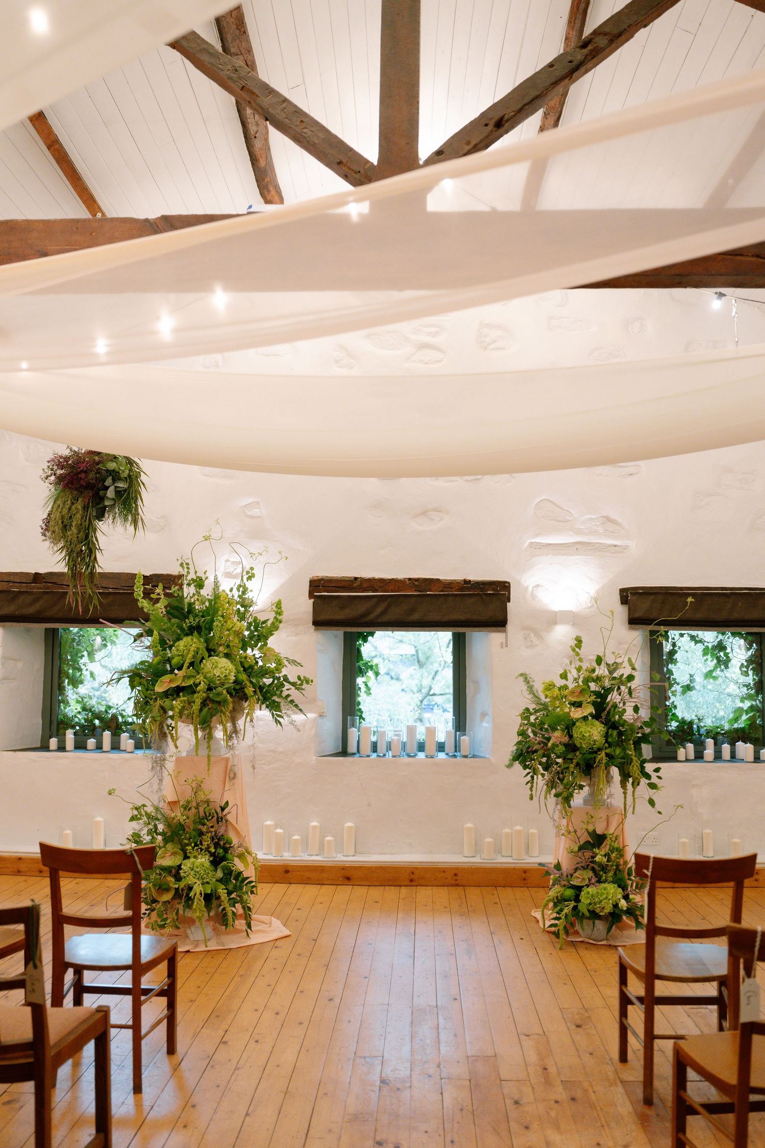 Rustic wedding venue interior with wooden beams, white walls, and hanging floral decorations.