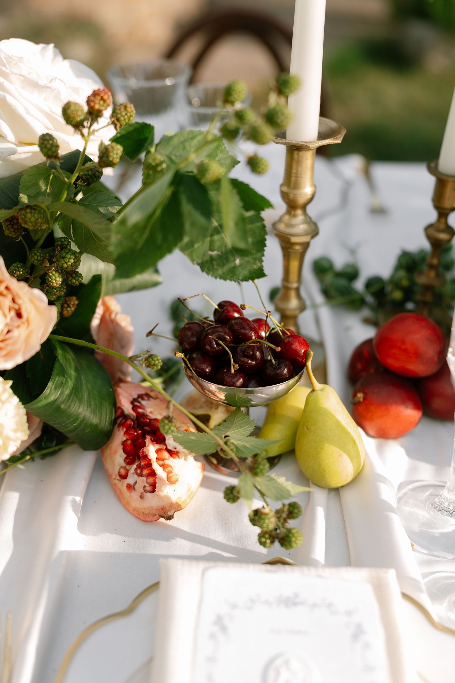 Elegant table setting with fresh fruits and white candles in brass holders.