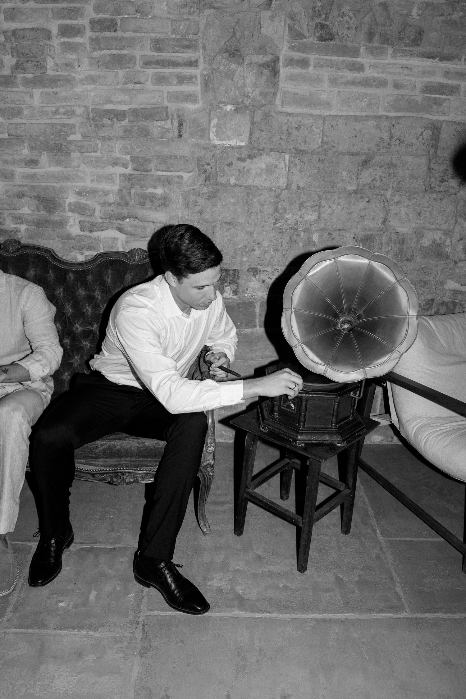 Black and white photo showing a phonograph with large horn speaker in front of a brick wall.