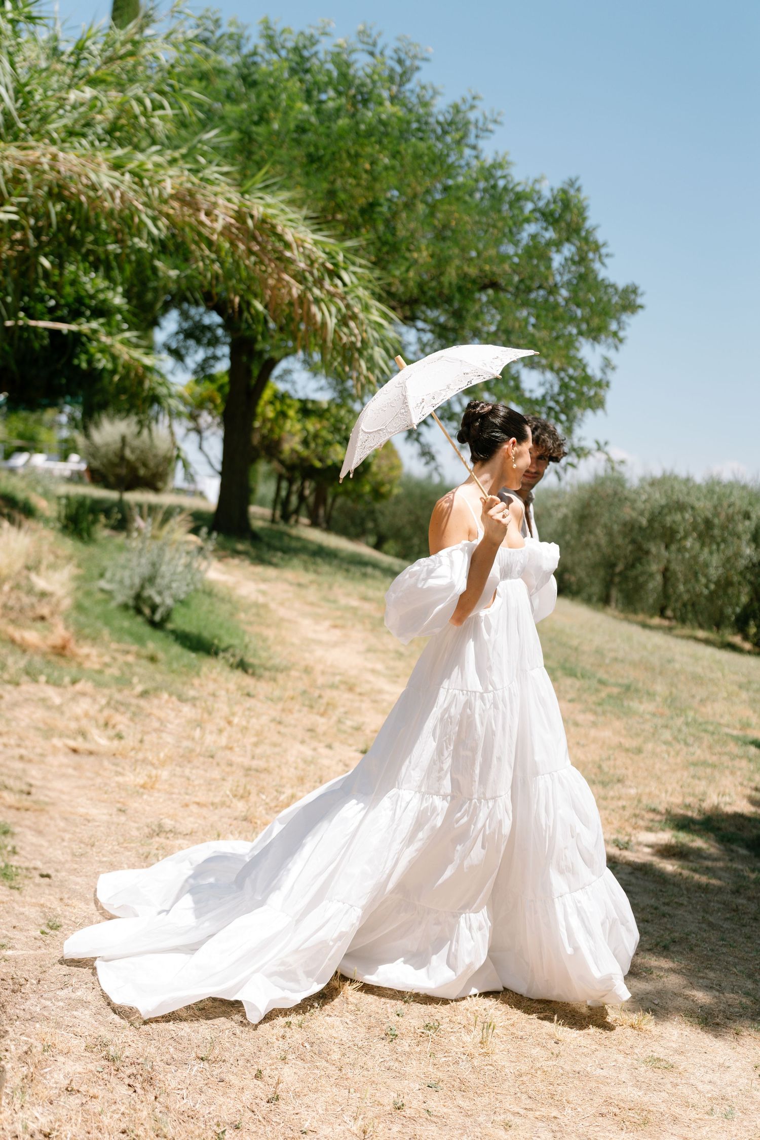 A flowing white dress twirls gracefully in an outdoor setting with olive trees.
