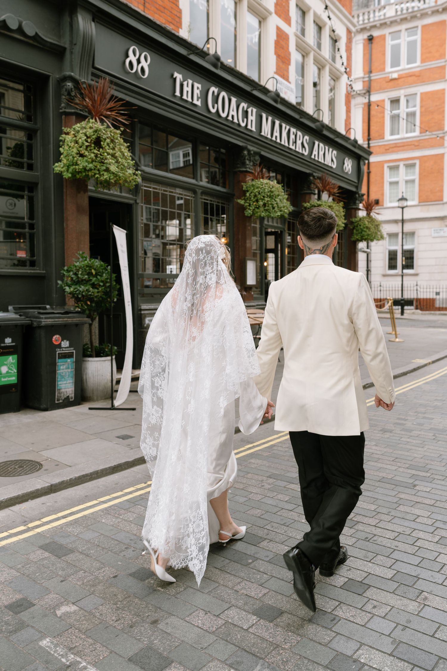 A couple walks hand in hand down a London street past The Coach Makers Arms pub.