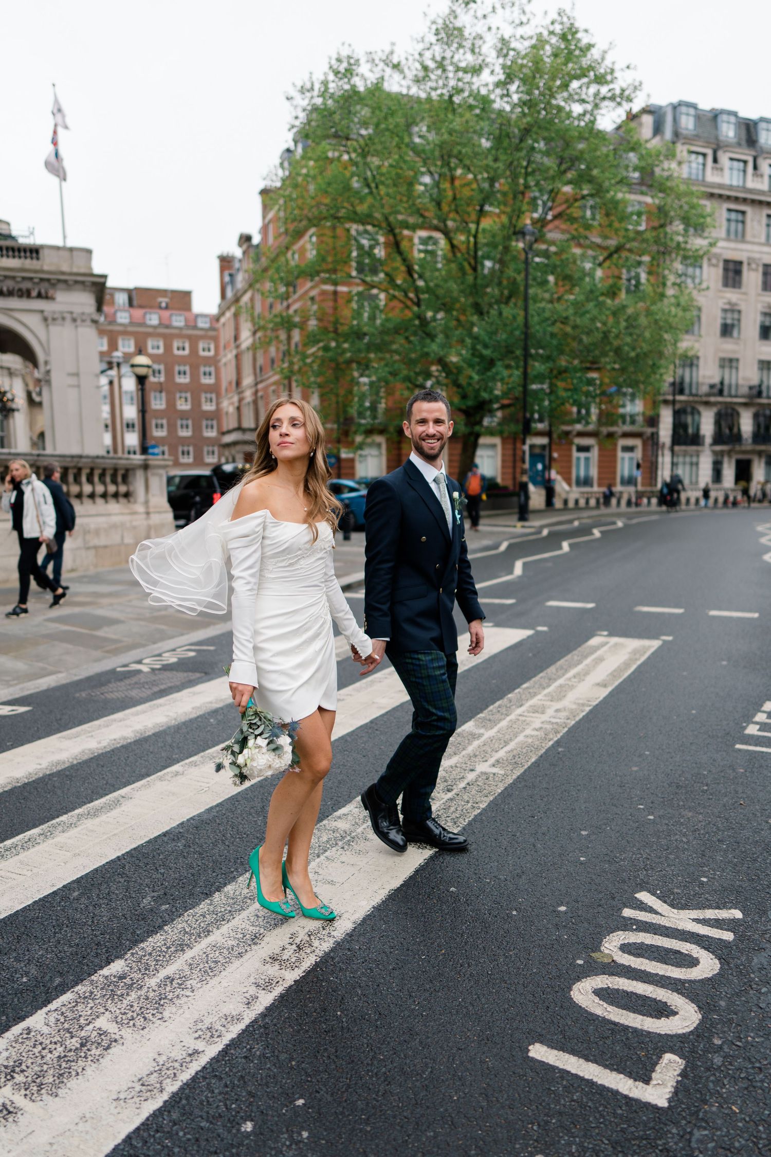 Wedding couple walks and dances across street markings in London.