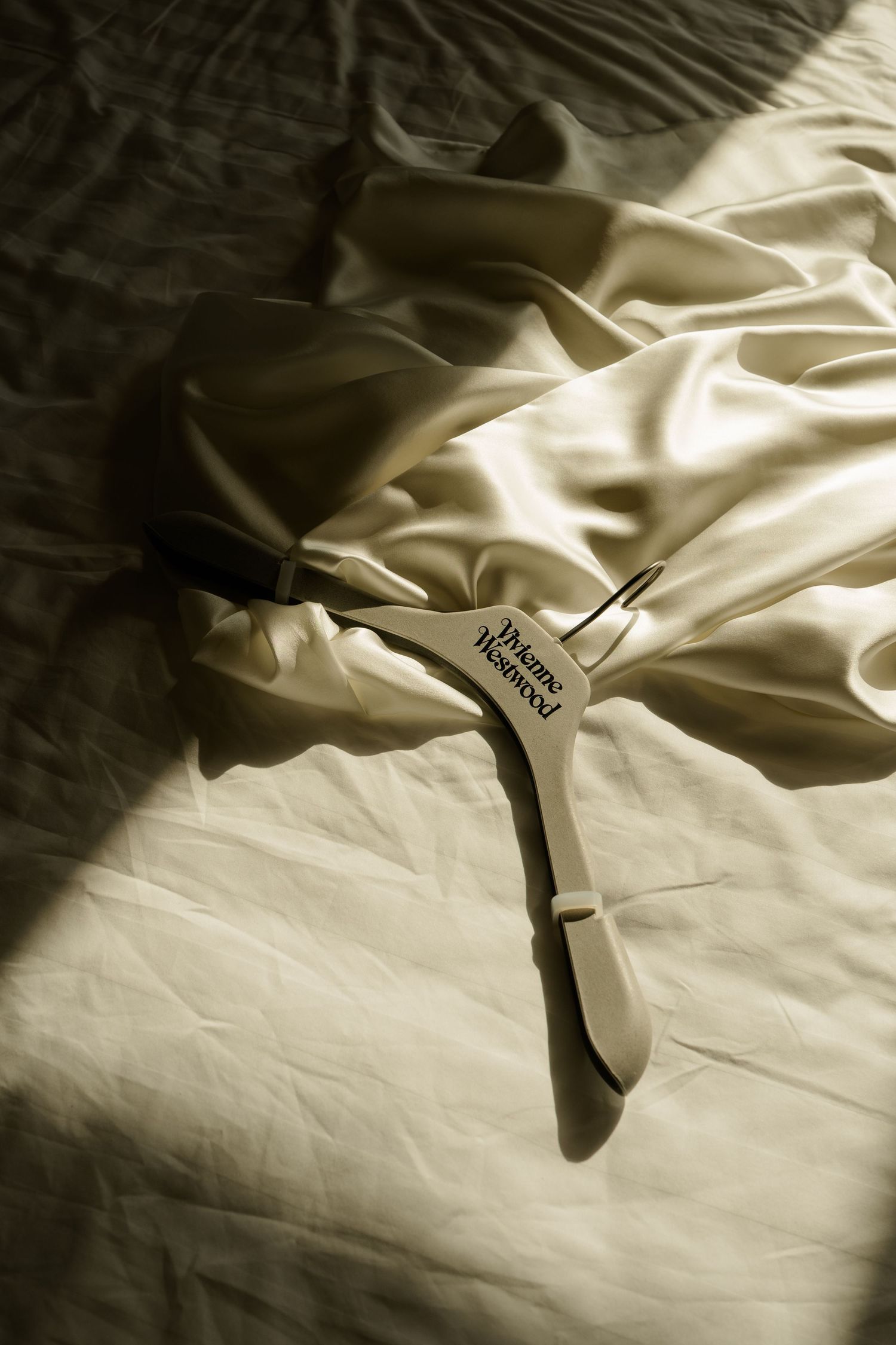 Vivienne Westwood branded hanger resting on a crumpled ivory satin dress laid on white bed sheets.