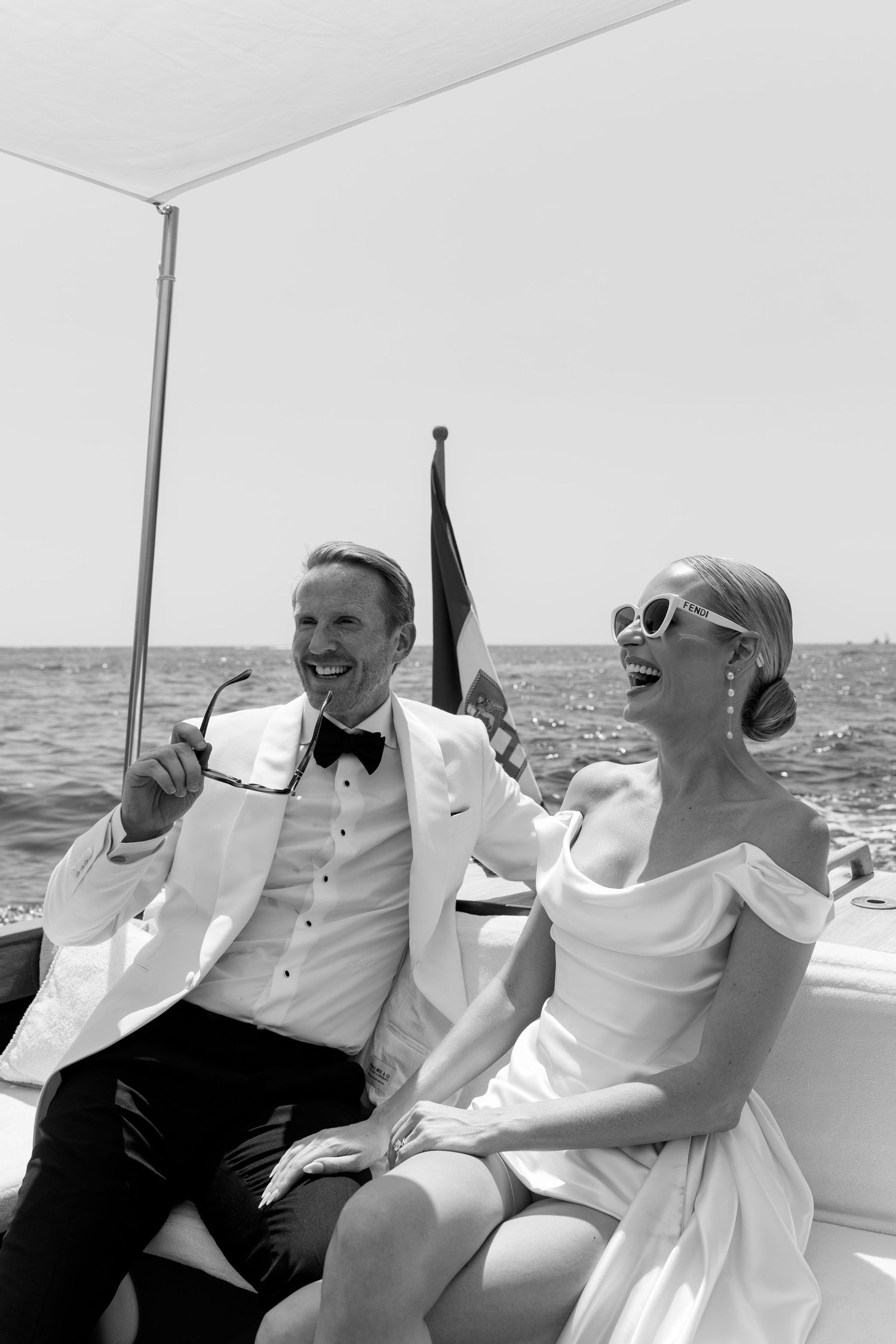 Laughing newlyweds in wedding attire enjoy a sunny boat ride on the open sea together.