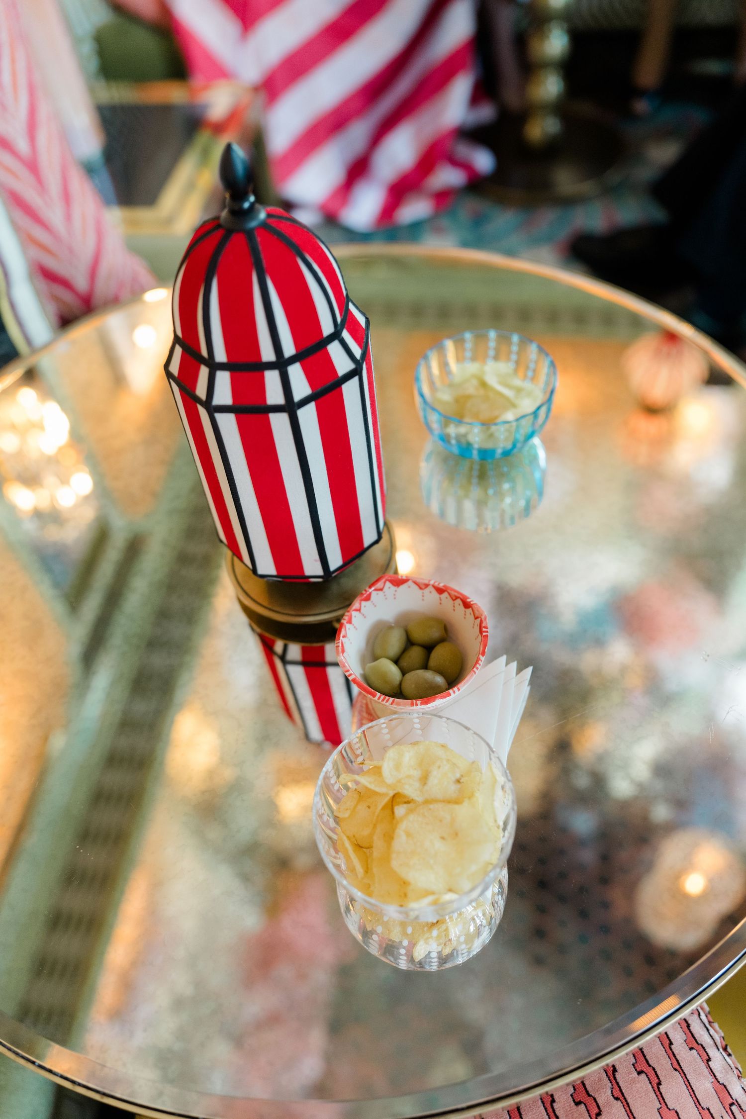 Overhead view of gold tray with striped lantern, olives, and crystal glass with chips.
