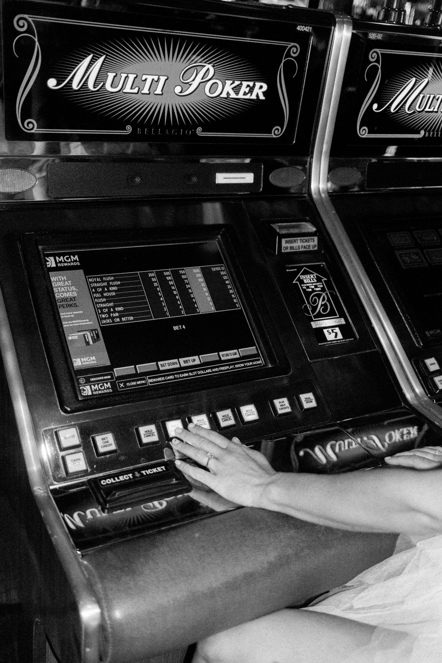 Close-up of hands playing a video poker machine in black and white.