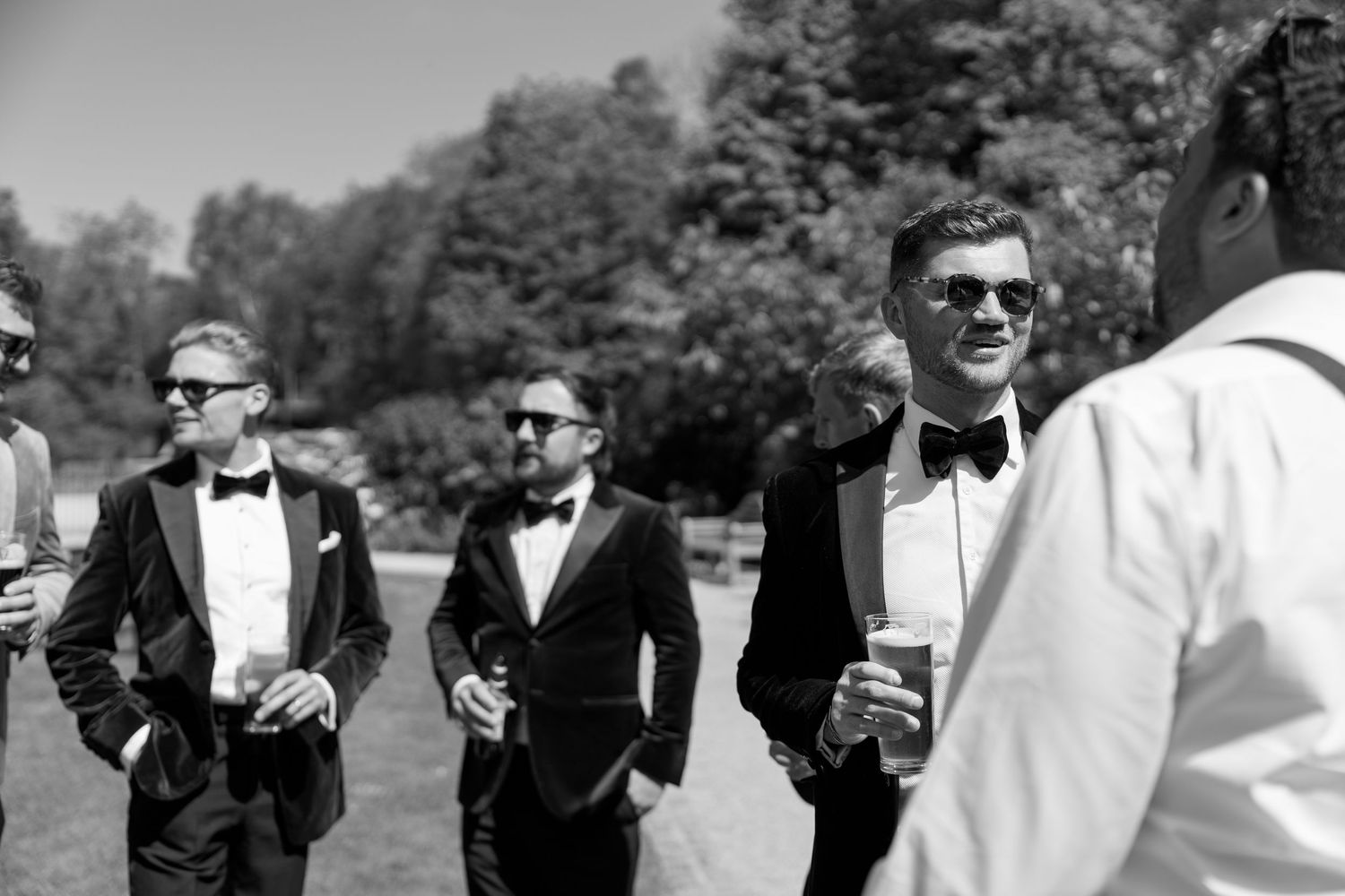 Groomsmen in formal attire mingling outdoors before ceremony.