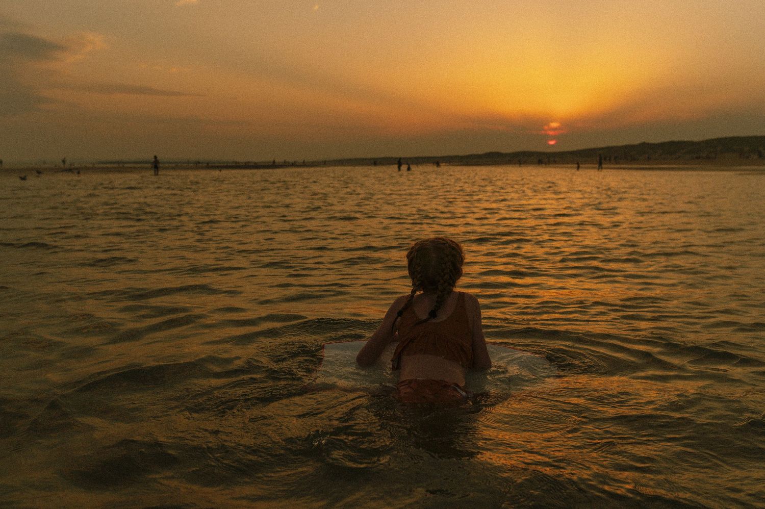 A silhouette wades in golden waters during a vibrant sunset.