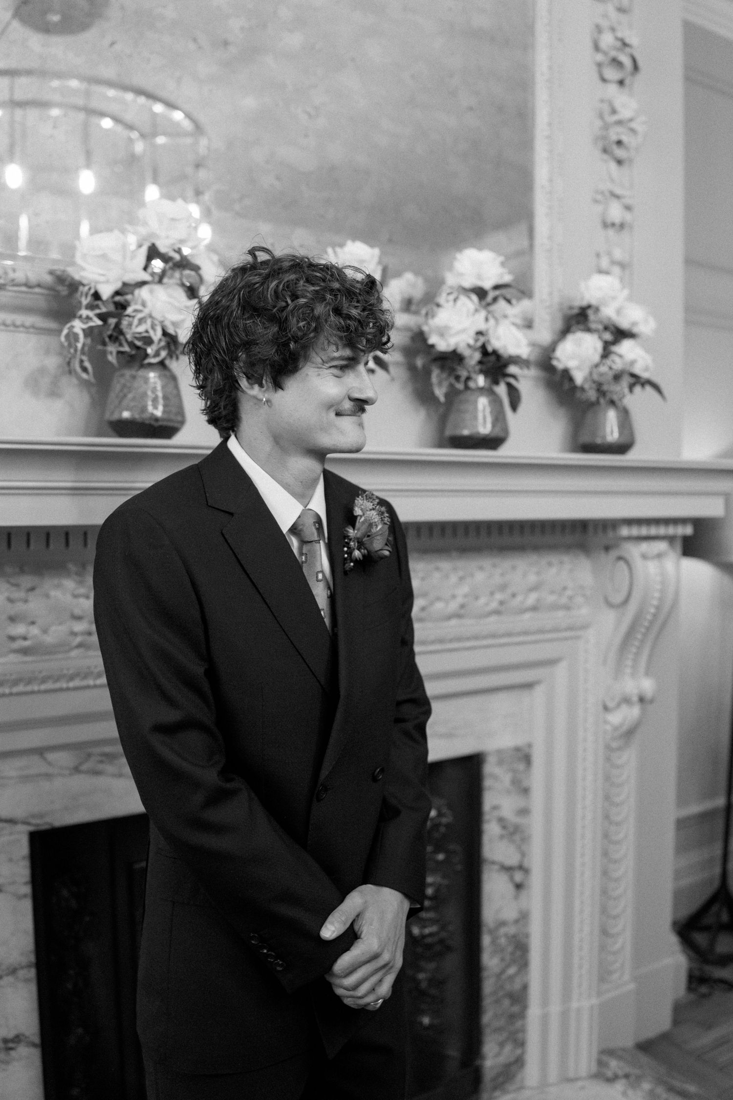 Person in formal attire standing beside decorated fireplace mantel at wedding.