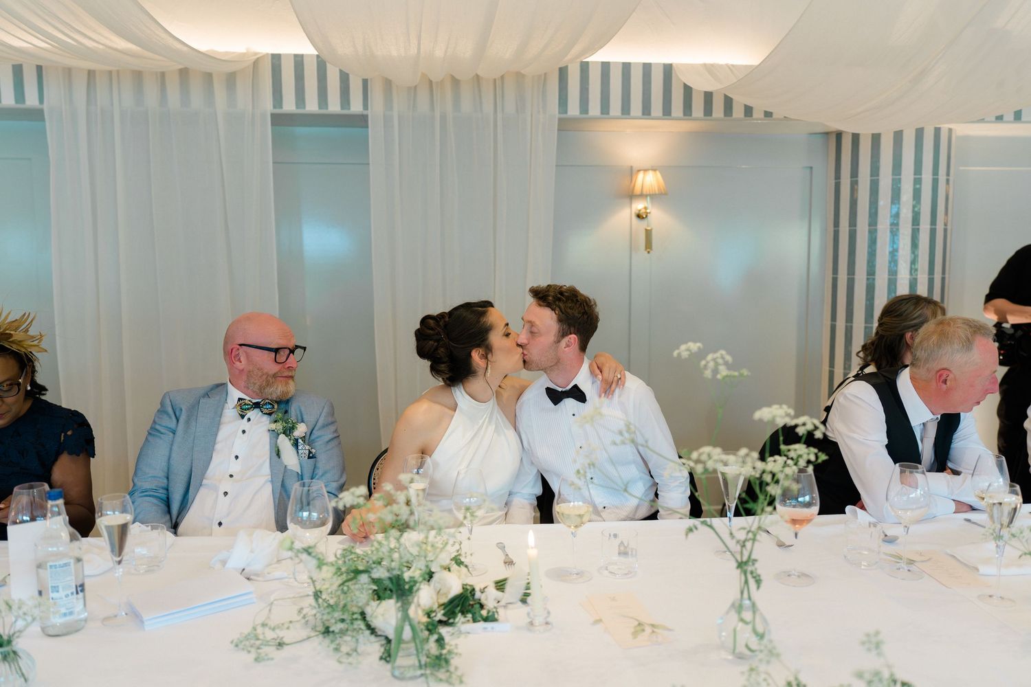 Bride and groom sharing a kiss at the head table during wedding reception.