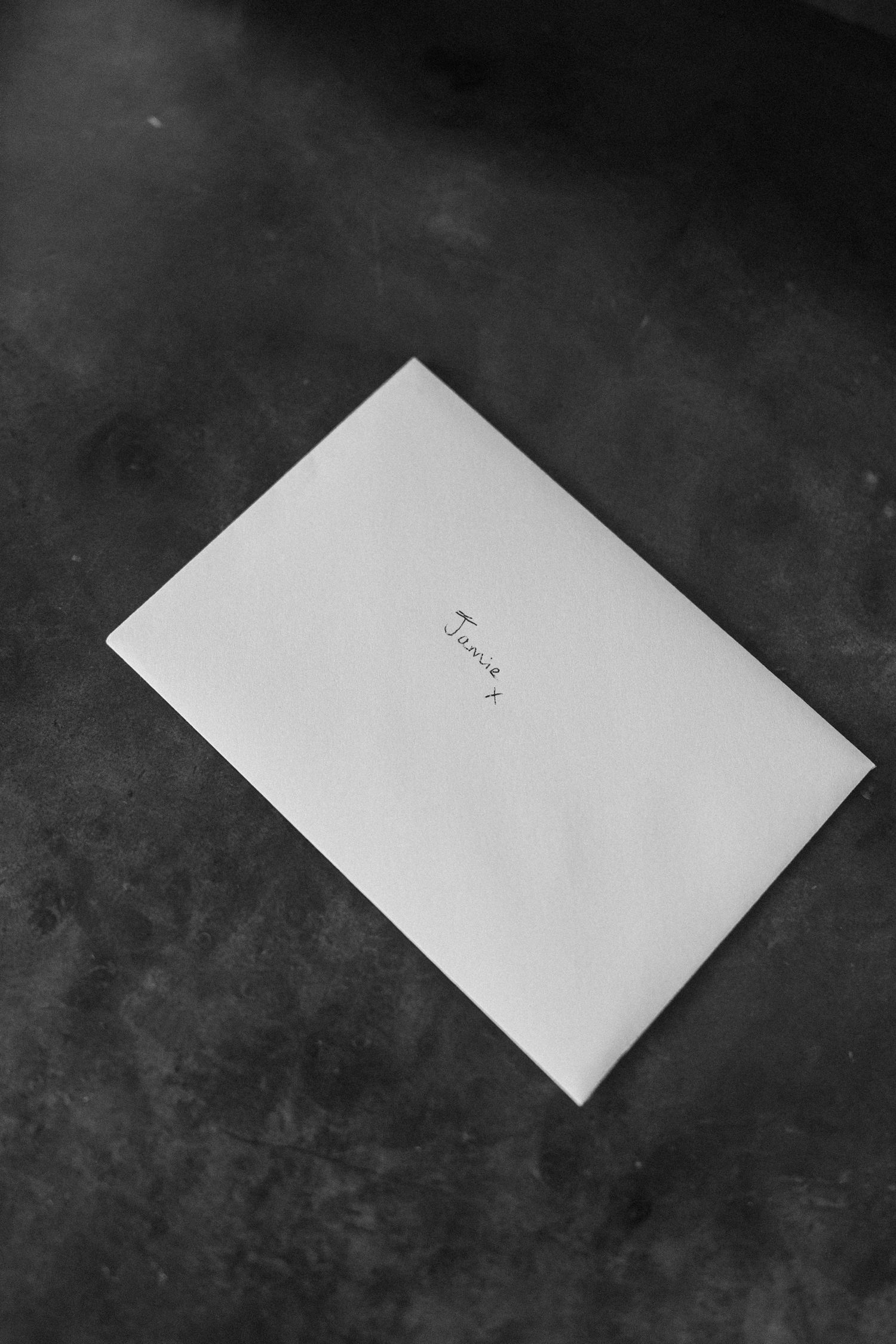 Minimalist black and white photo of a white envelope addressed to Jenny on a dark textured surface.