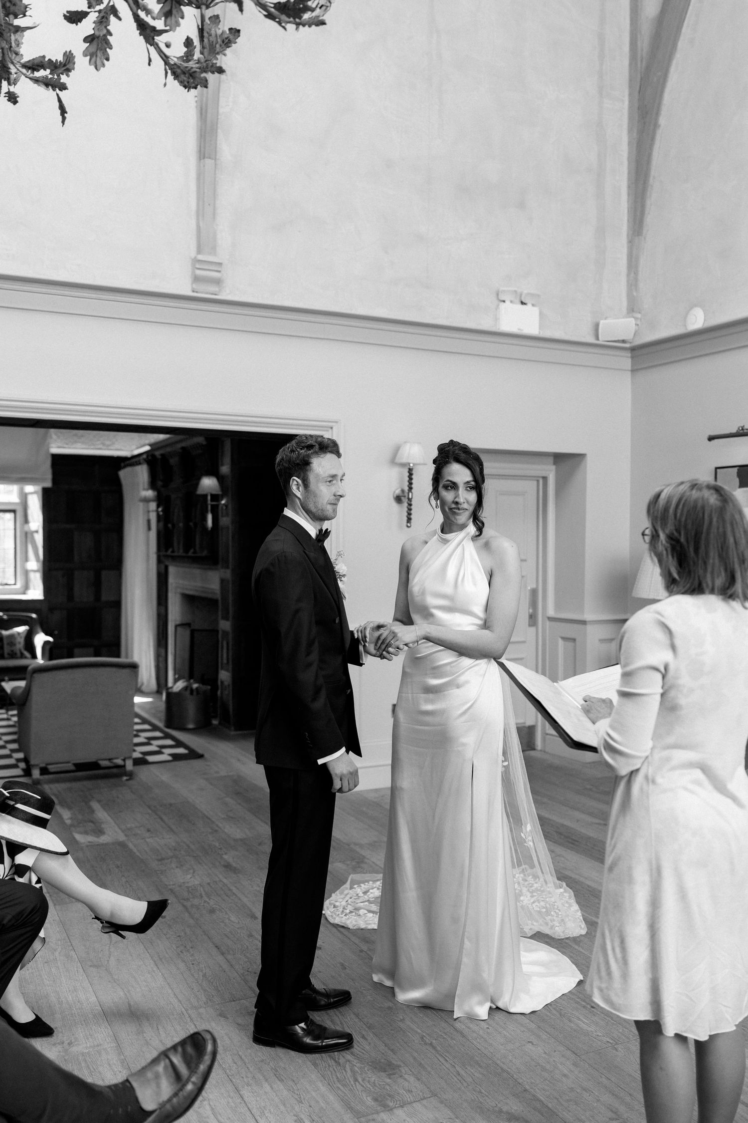 Bride and groom hold hands facing each other during wedding ceremony with officiant reading vows.