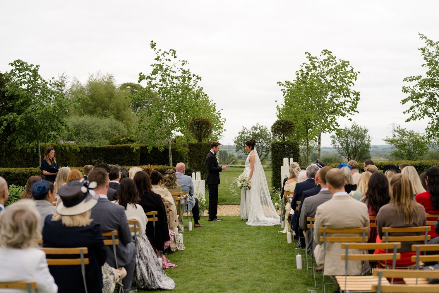 Bride and groom exchange vows at outdoor garden wedding ceremony with seated guests.