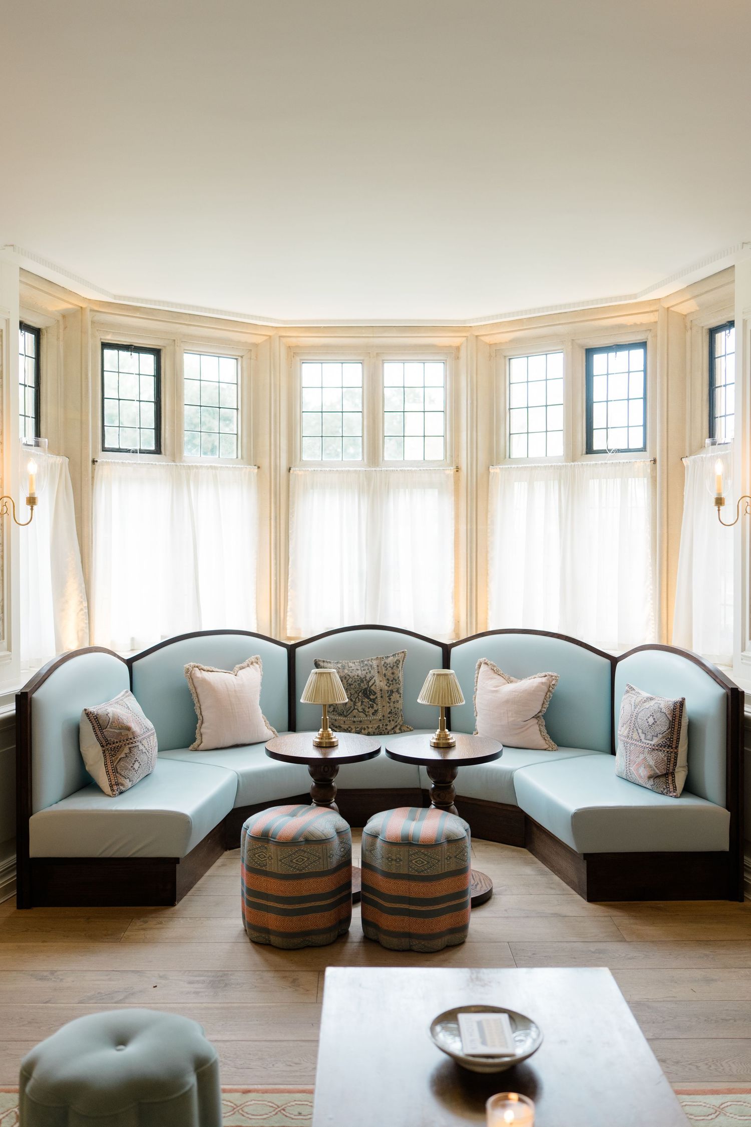 Elegant curved banquette seating in light blue upholstery with dark wood trim in a bay window sitting room.