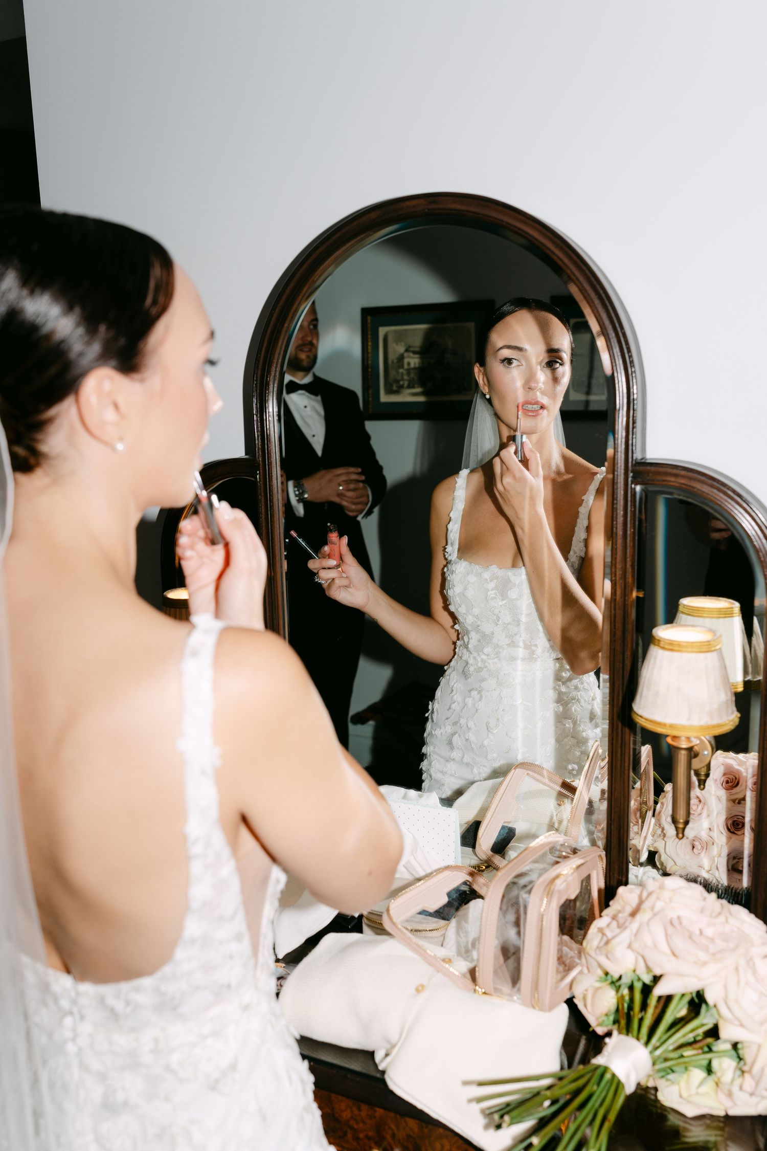 Bride applies makeup in front of ornate mirror during wedding preparations.