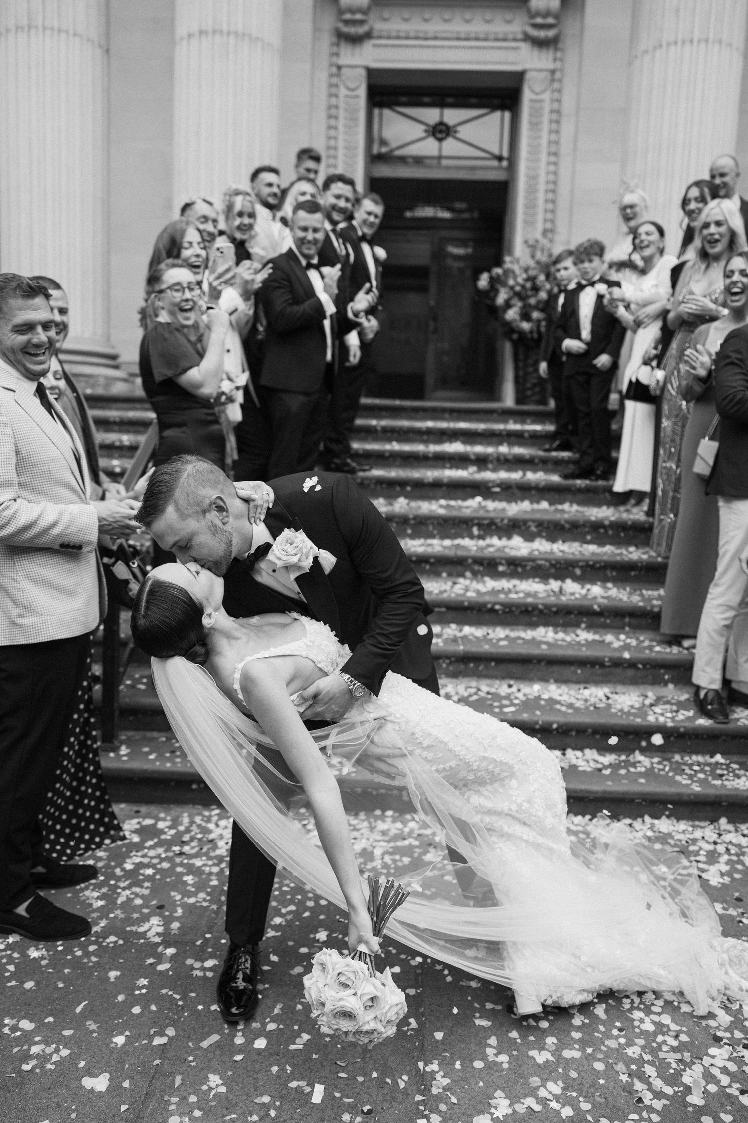 A romantic wedding moment captured in black and white as a couple dips during their first dance with flower petals scattered around.
