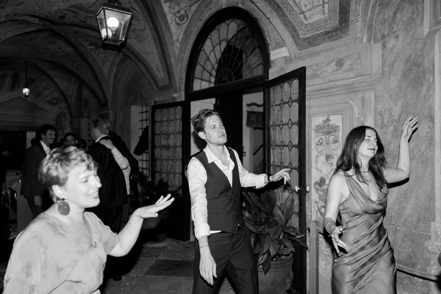 Partygoers dancing beneath vintage light fixtures in a classical architectural space.