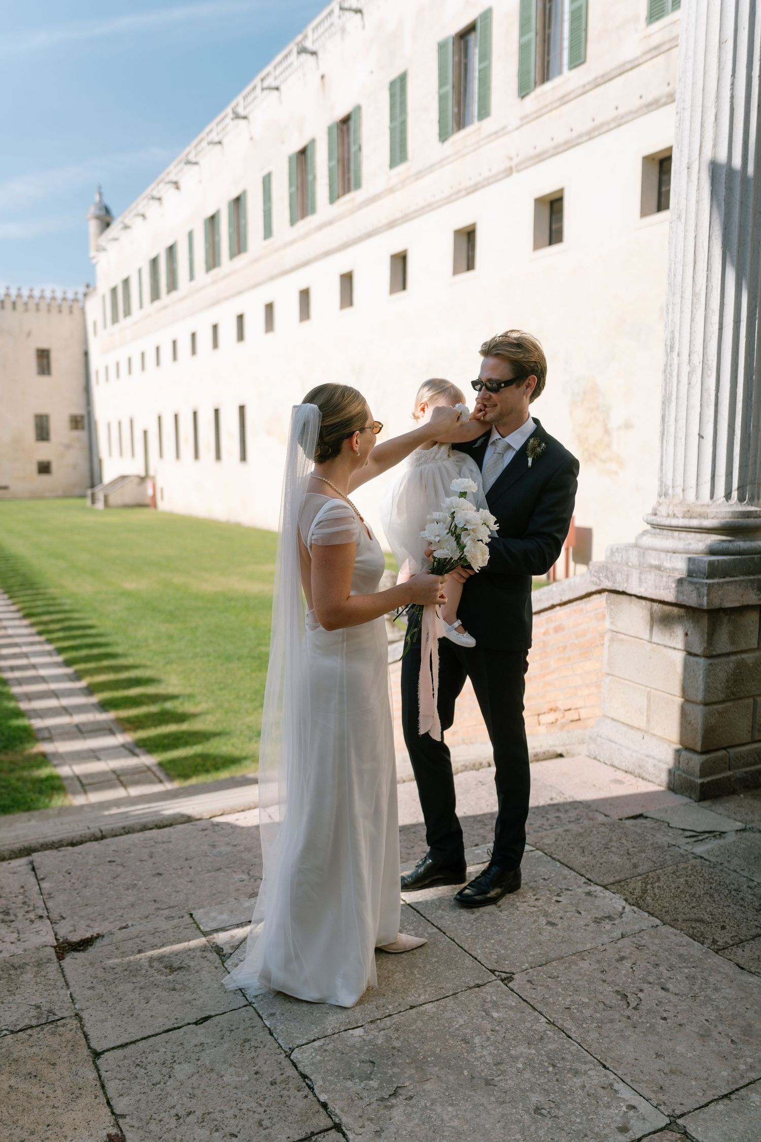 Wedding couple shares intimate moments against a white architectural backdrop with columns.