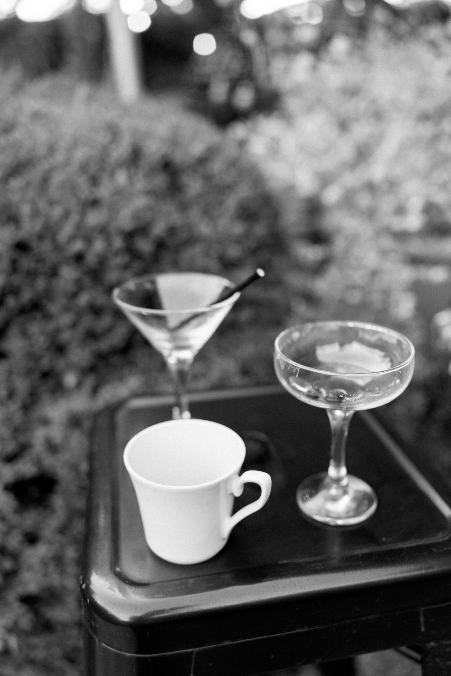 Black and white photo of cocktail glasses and coffee cups arranged on dark serving trays.