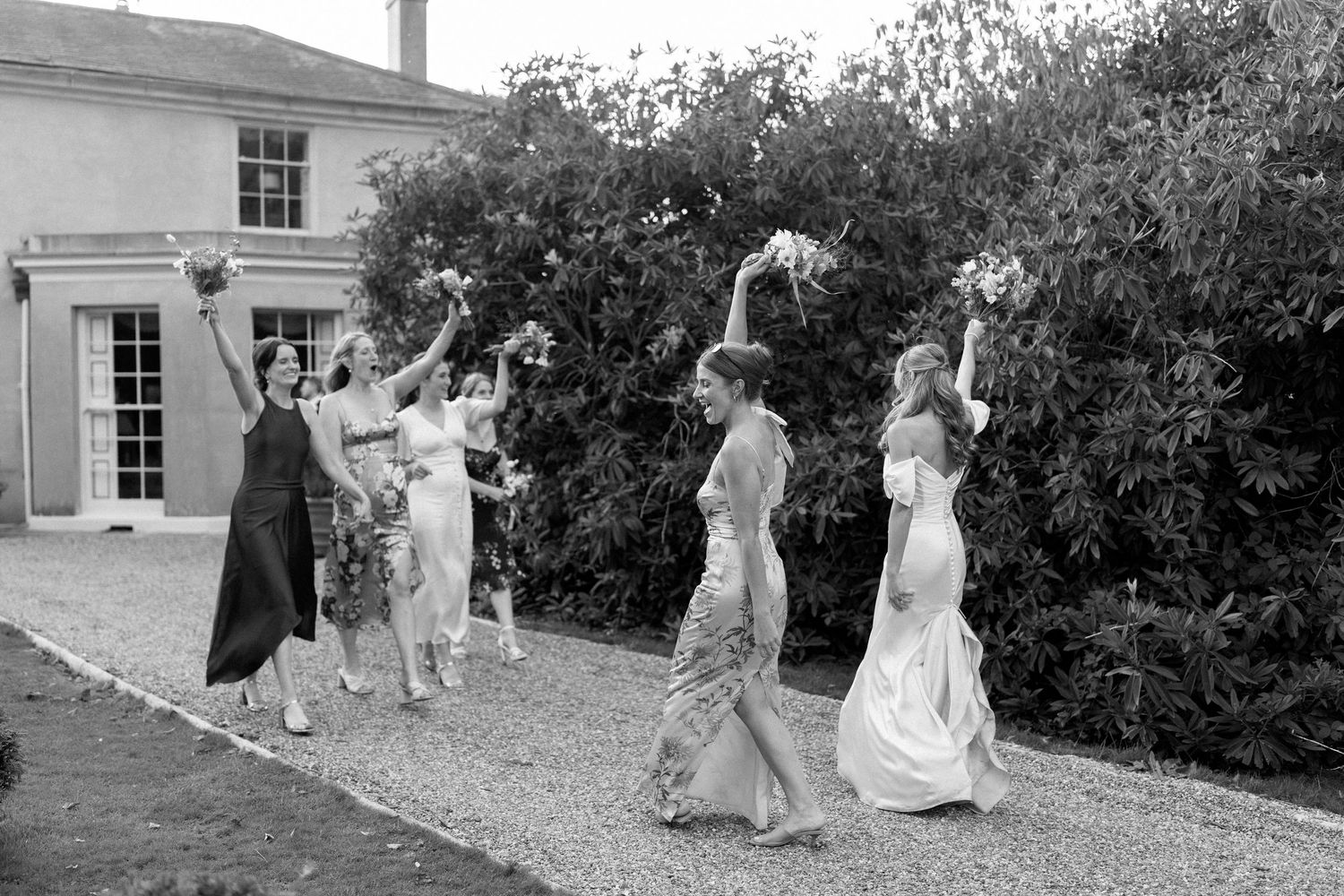 Black and white photo of wedding party walking along path beside historic building.