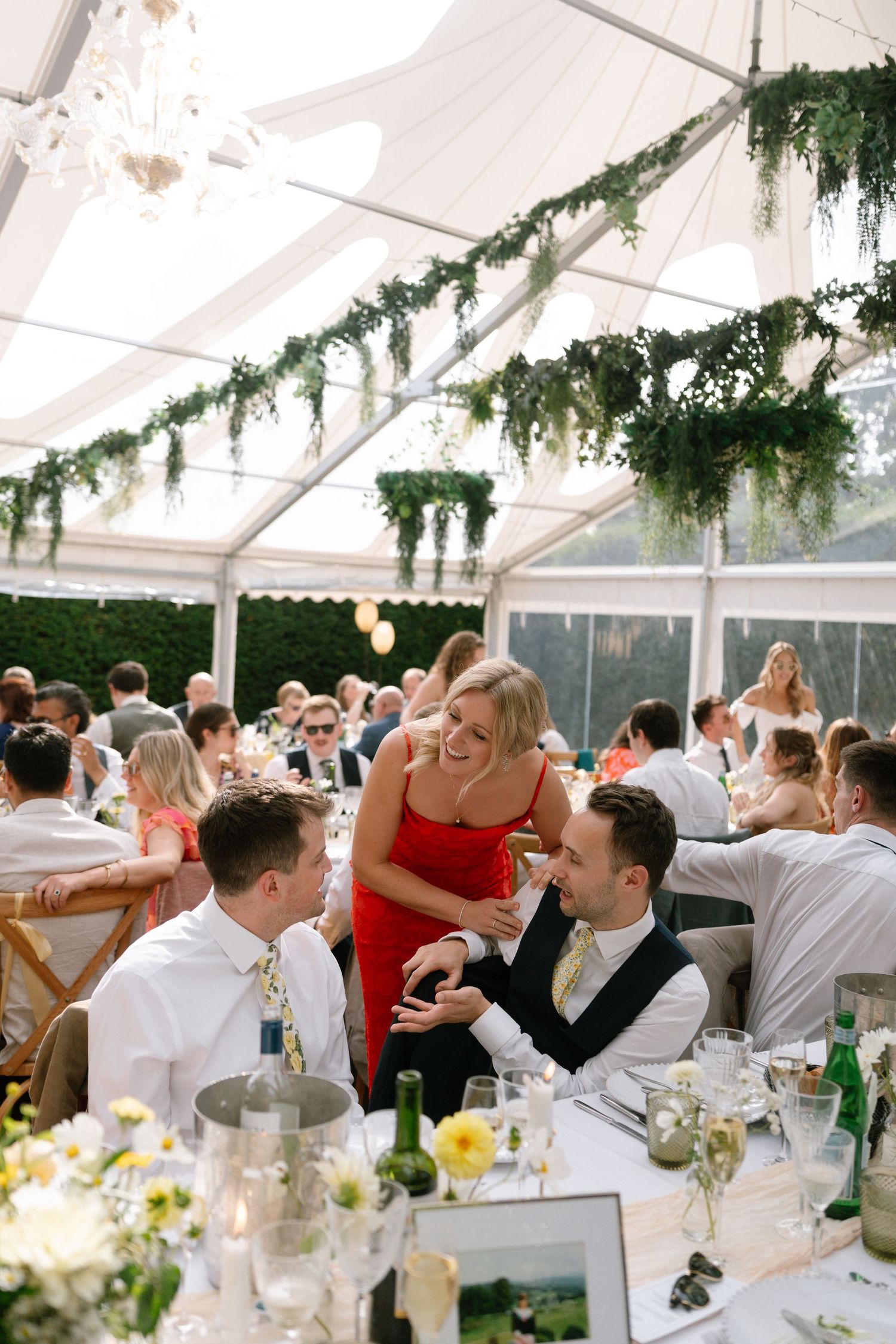 Wedding reception in a bright greenhouse tent with guests dining at decorated tables.