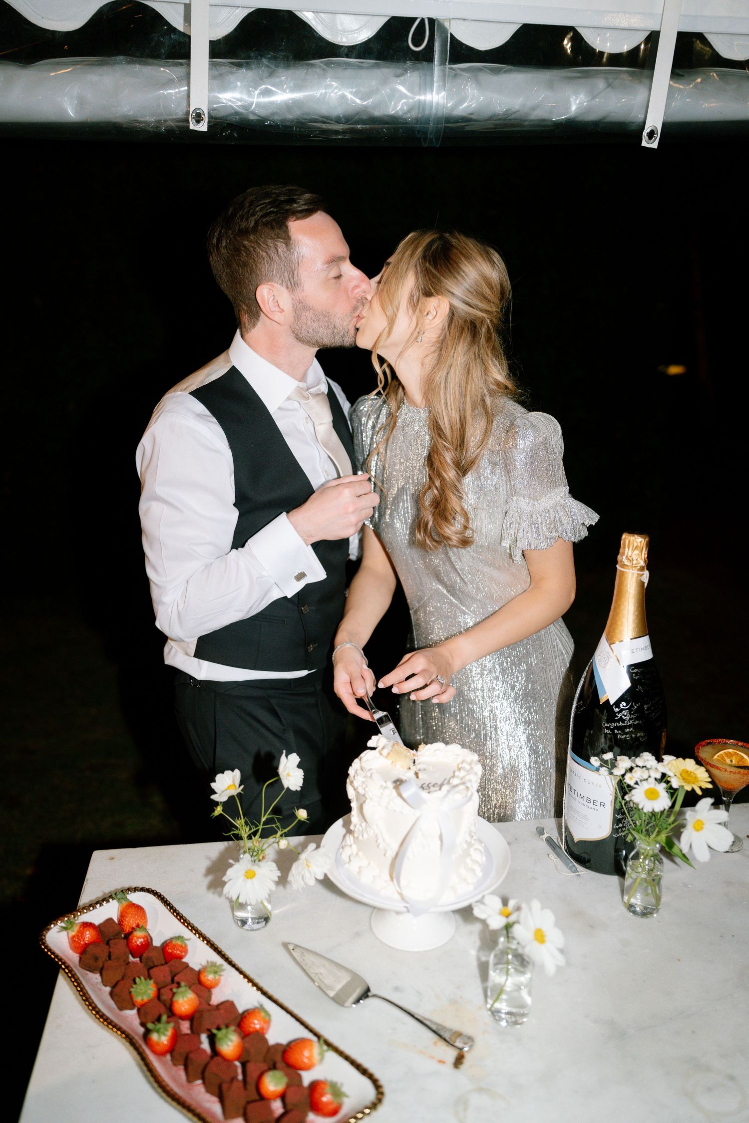 A couple celebrates at their wedding reception table with strawberries and champagne.