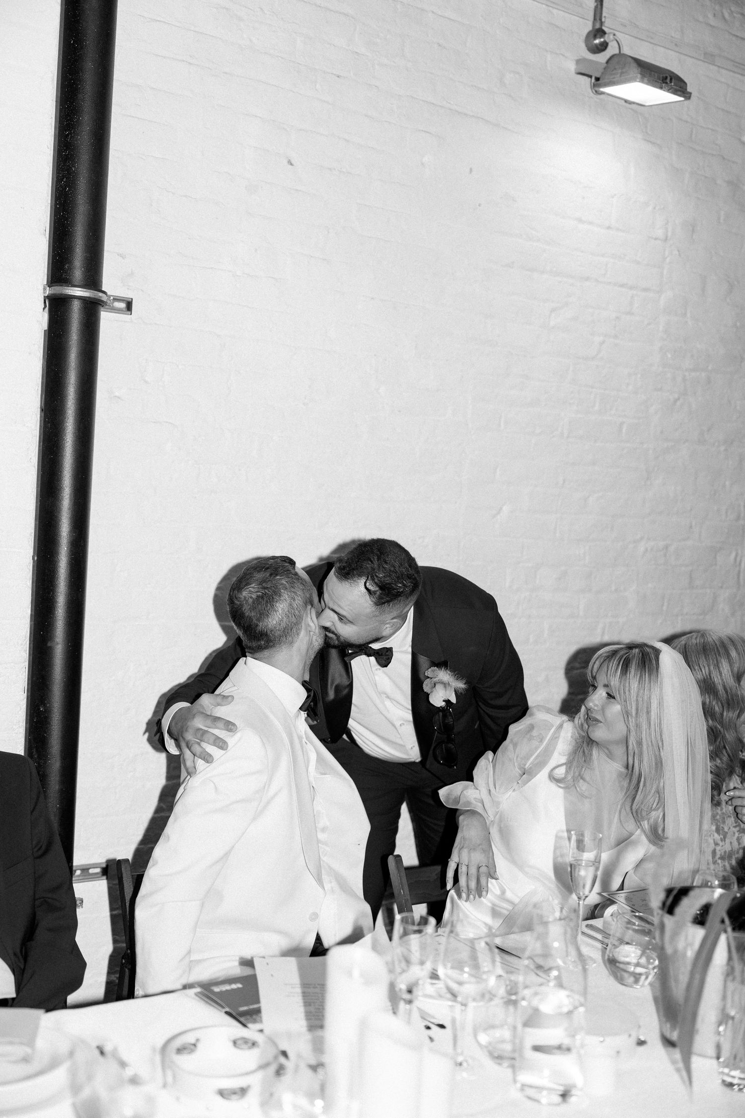 Black and white photo of wedding guests dining and socializing at a long table.