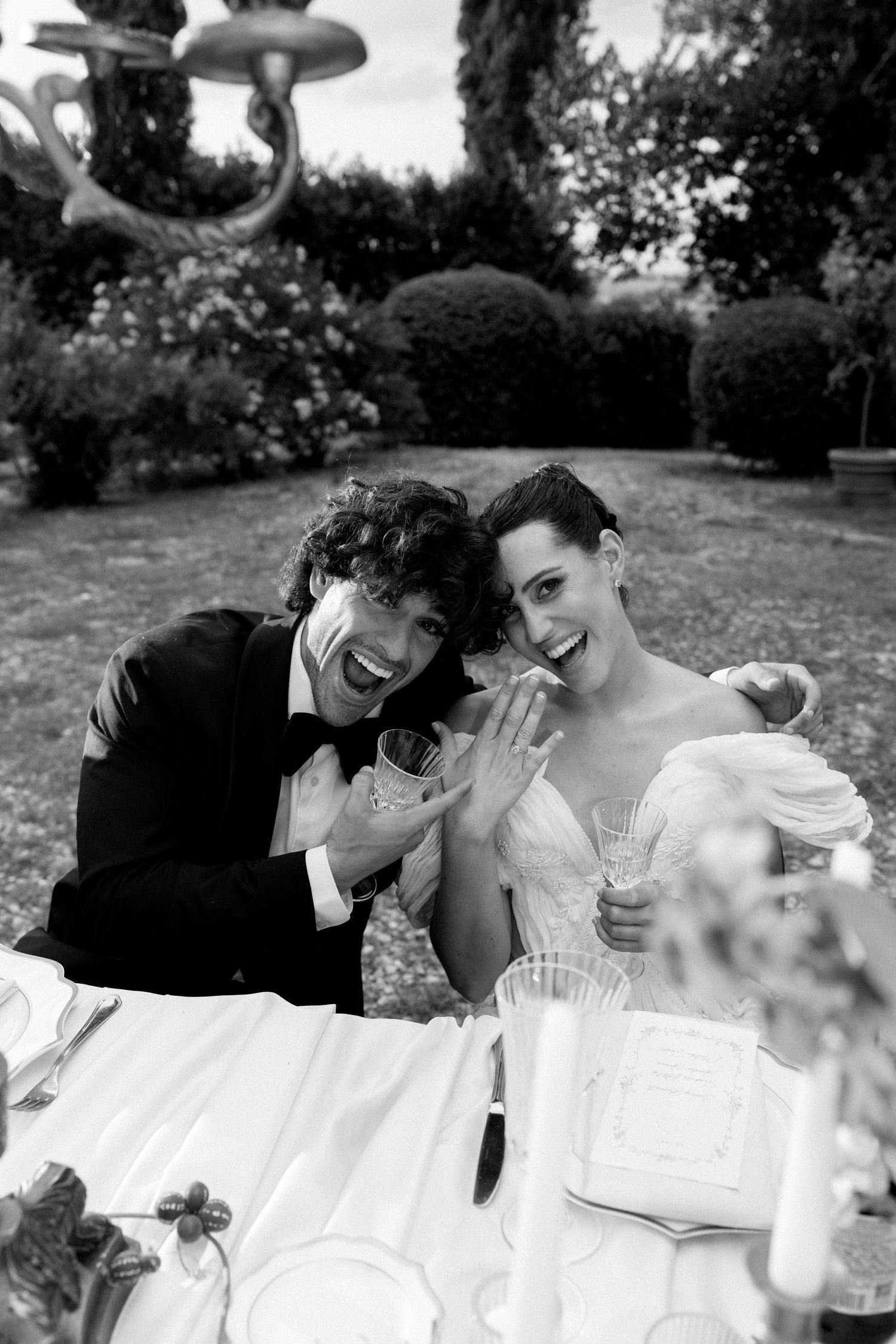 A black and white photo of a joyful couple celebrating at an outdoor wedding reception.