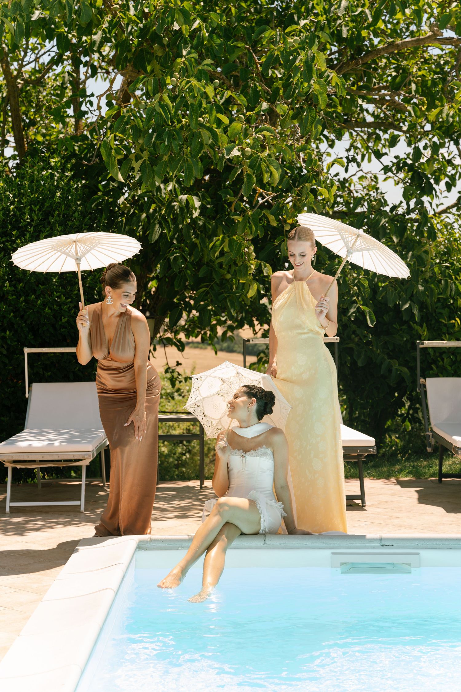 People with parasols enjoying a poolside gathering in a lush garden setting.