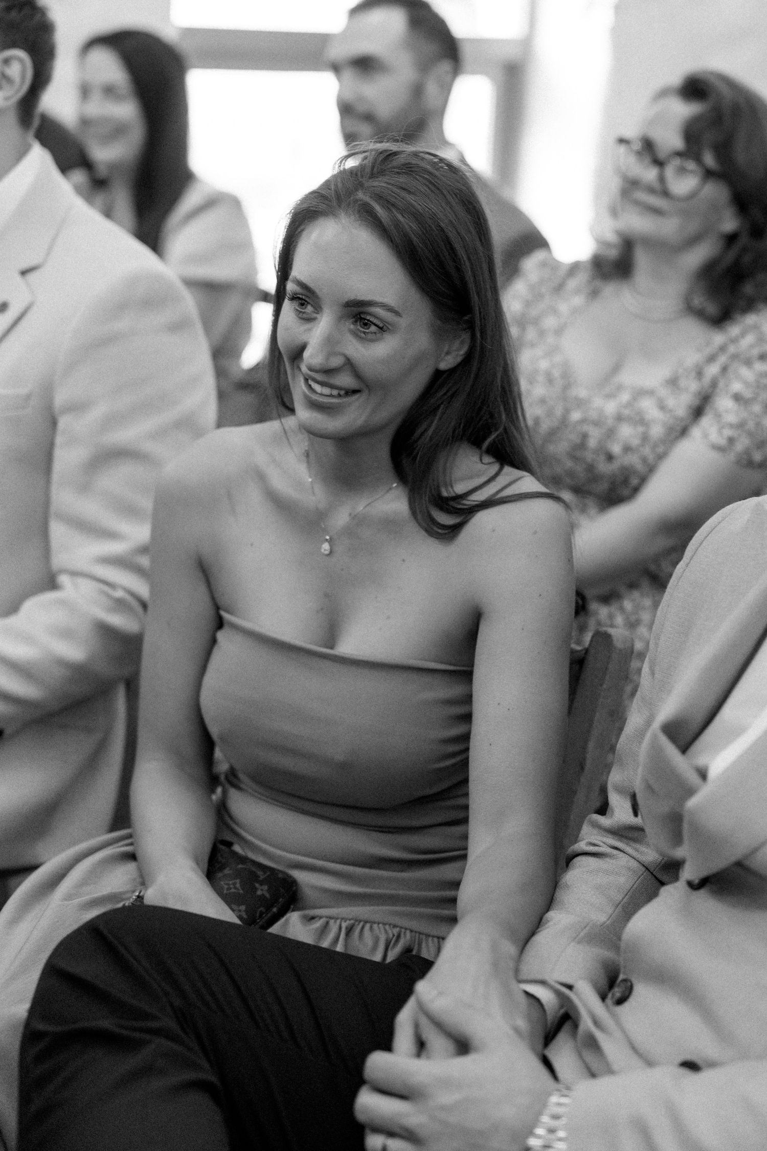 Wedding guests in formal attire smile and laugh during a celebration.