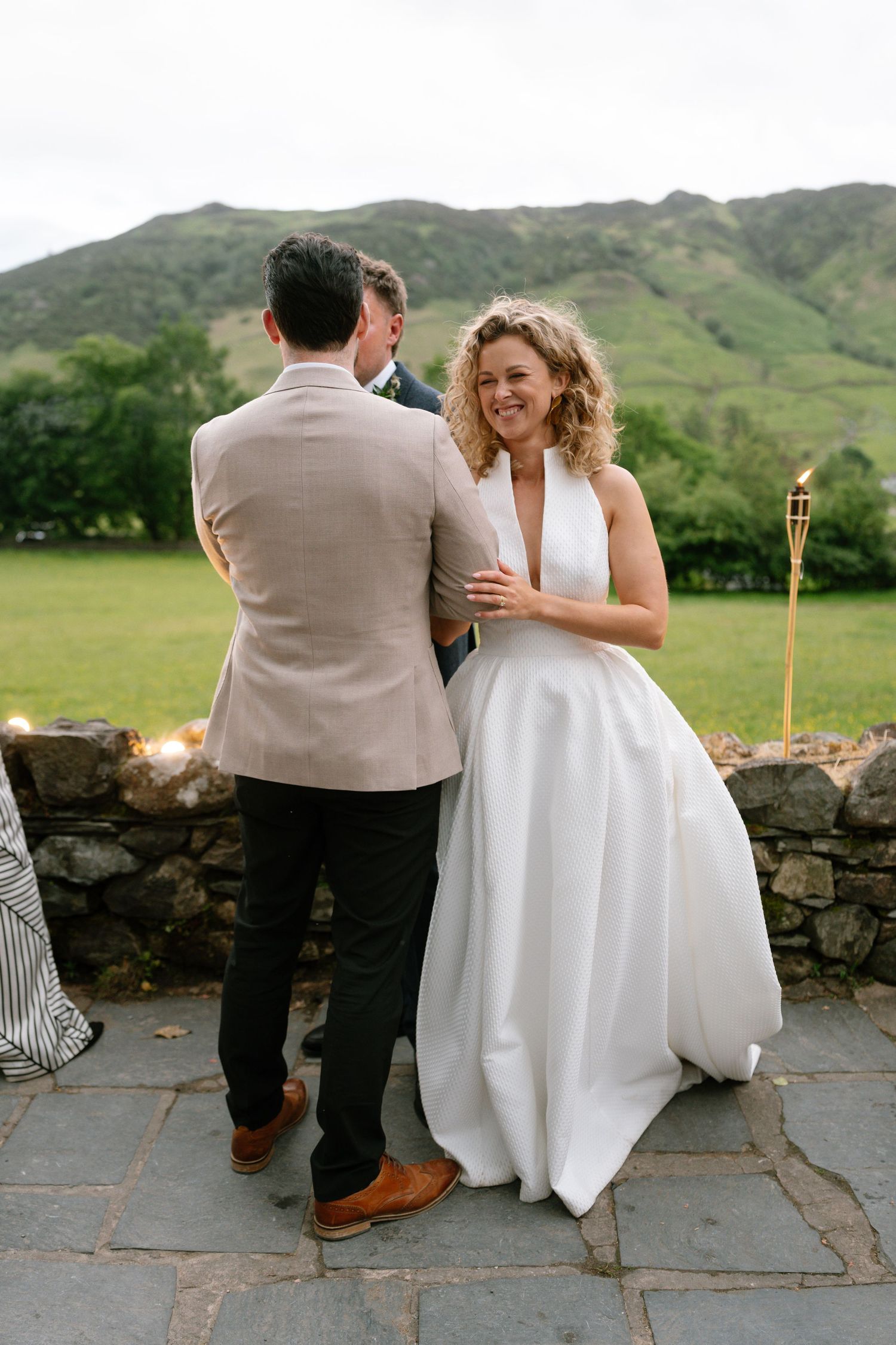 Wedding couple sits together on stone steps with mountain views and tiki torches.