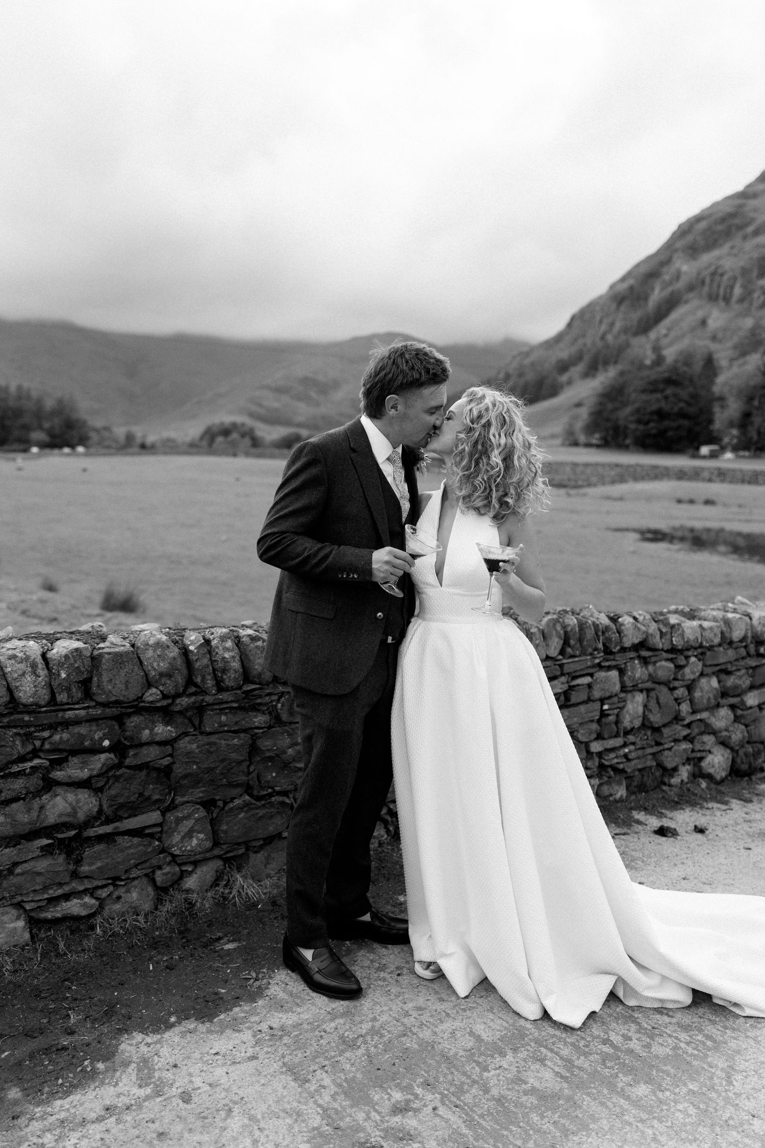 Romantic black and white wedding portraits by stone wall with mountain landscape.