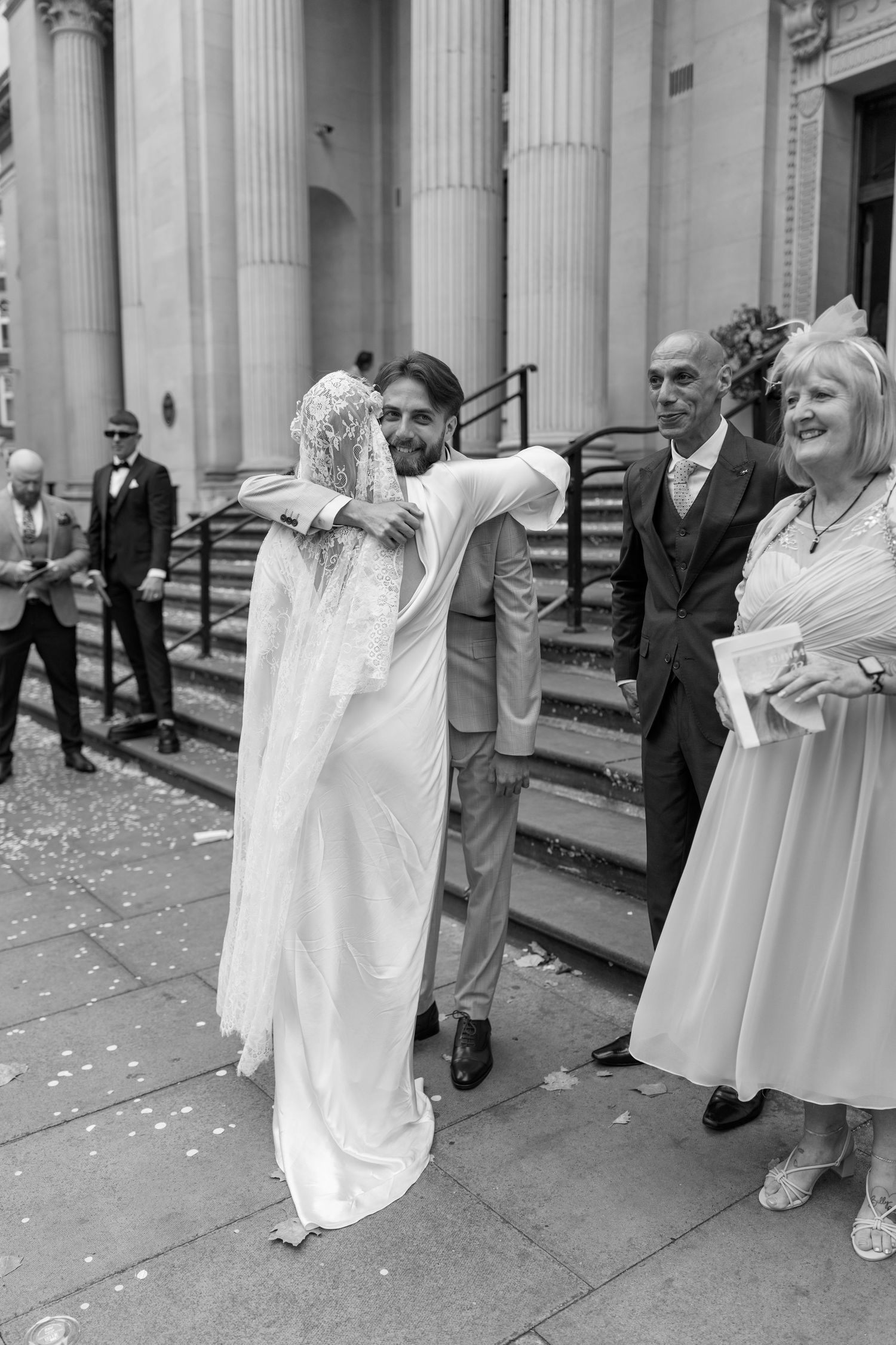 Wedding celebration captured in black and white on the steps of a historic building with classical columns.