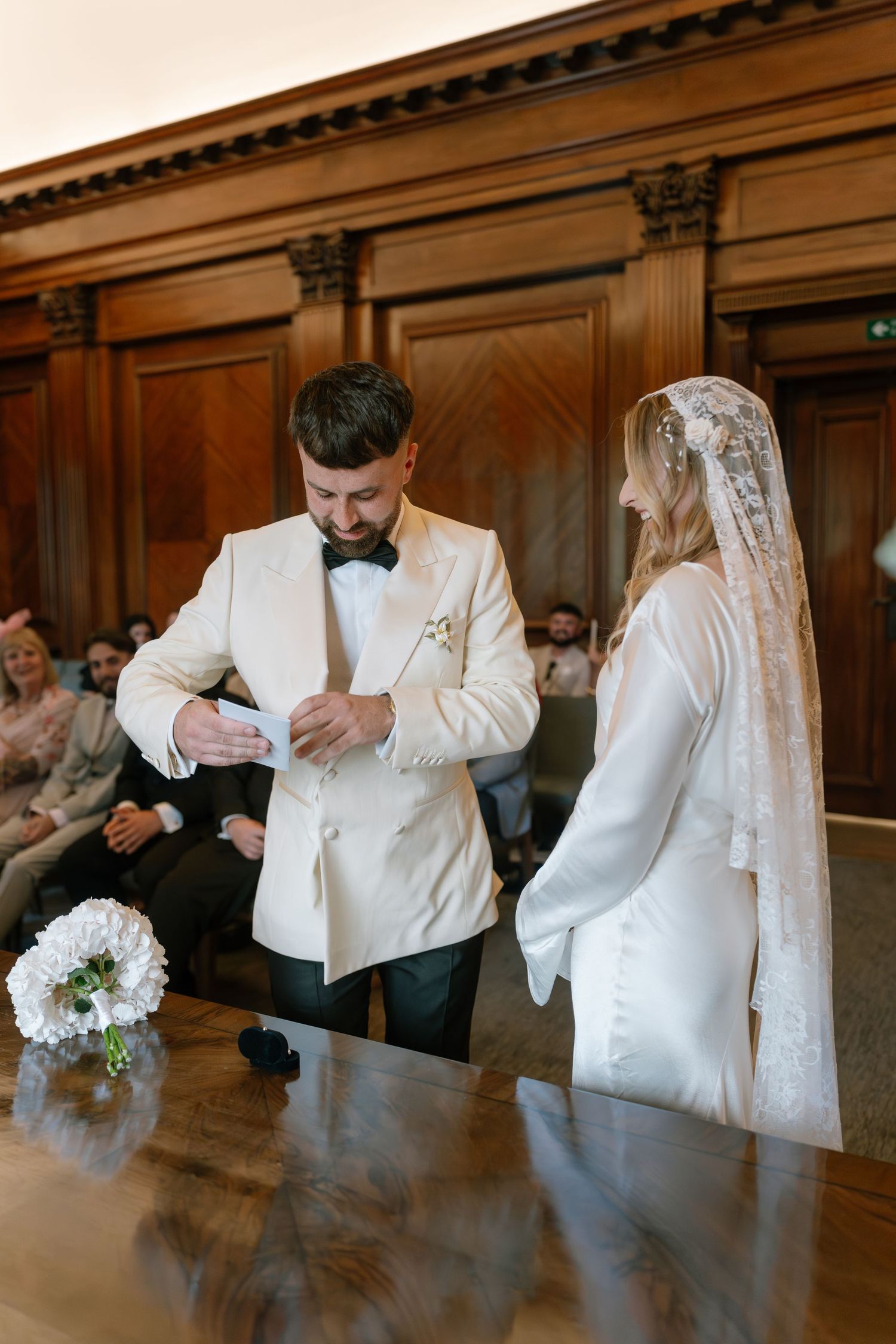 A couple stands at an altar during their wedding ceremony in a classic wood-paneled venue.