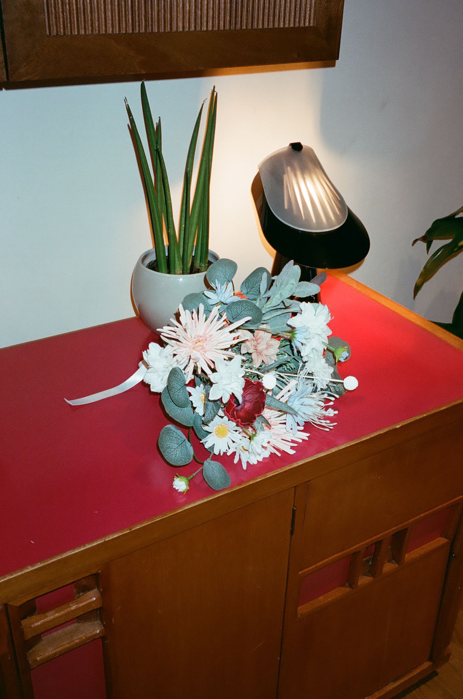 A decorative arrangement of white paper flowers and turquoise accents sits atop a wooden cabinet in low light.