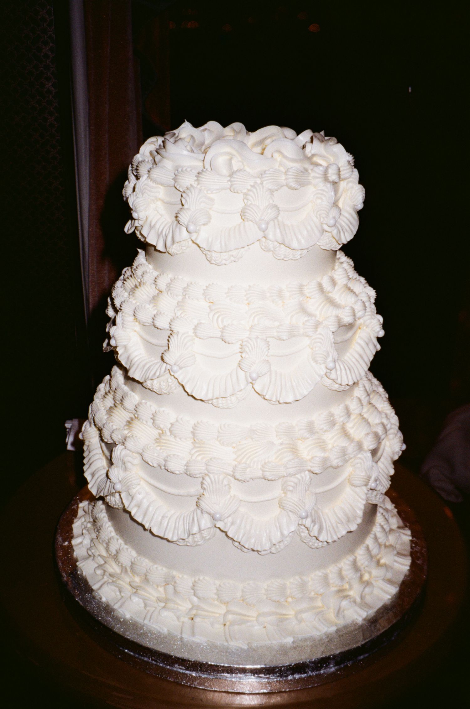 A traditional white wedding cake decorated with intricate piped frosting details and delicate rosettes on multiple tiers.