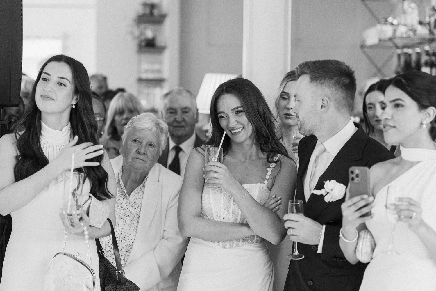 Black and white photo of bride and groom celebrating with guests holding champagne glasses.