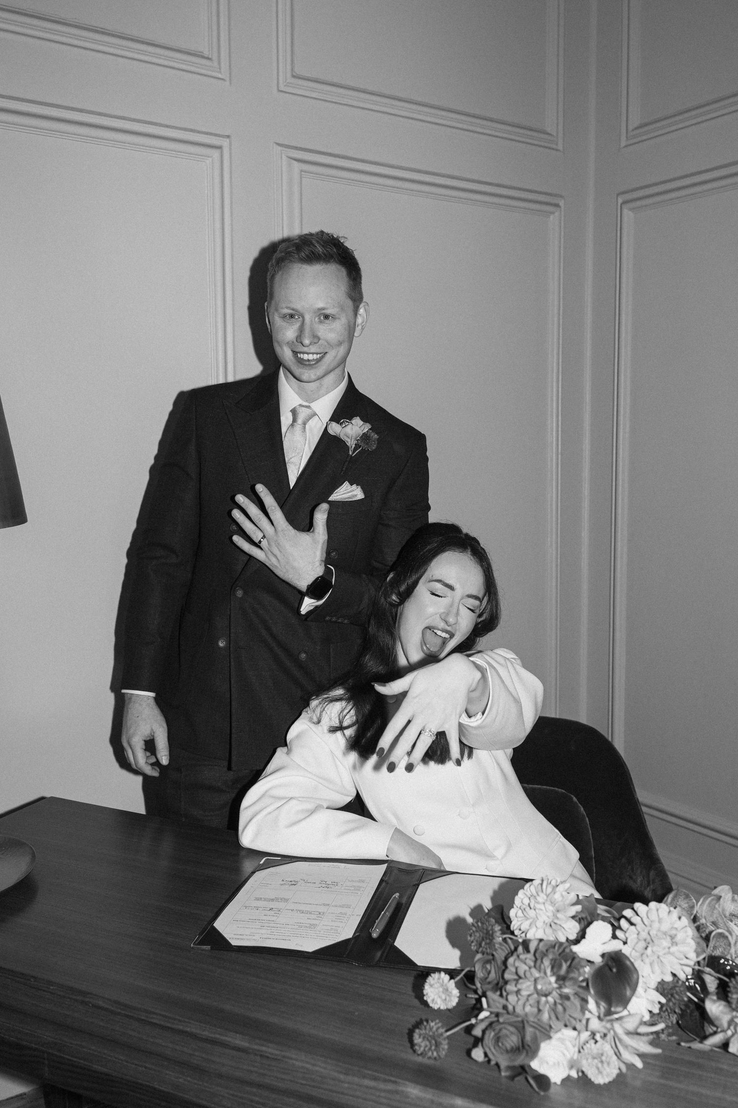 Black and white photo of newlyweds laughing after signing wedding register at registry office.