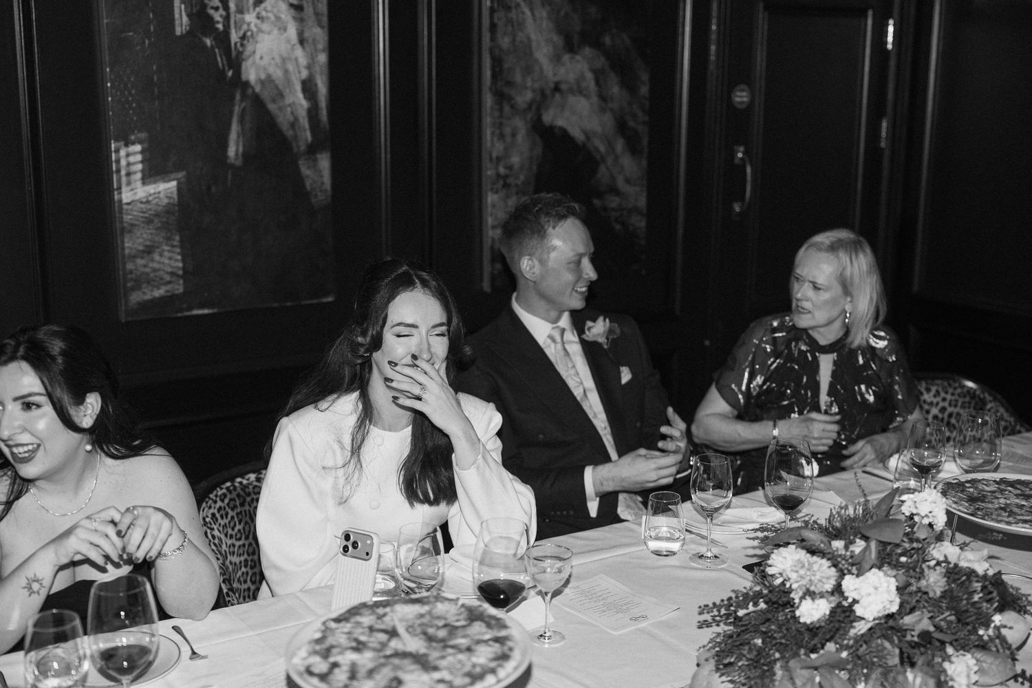 Wedding party laughing at dinner reception table in black and white photo.
