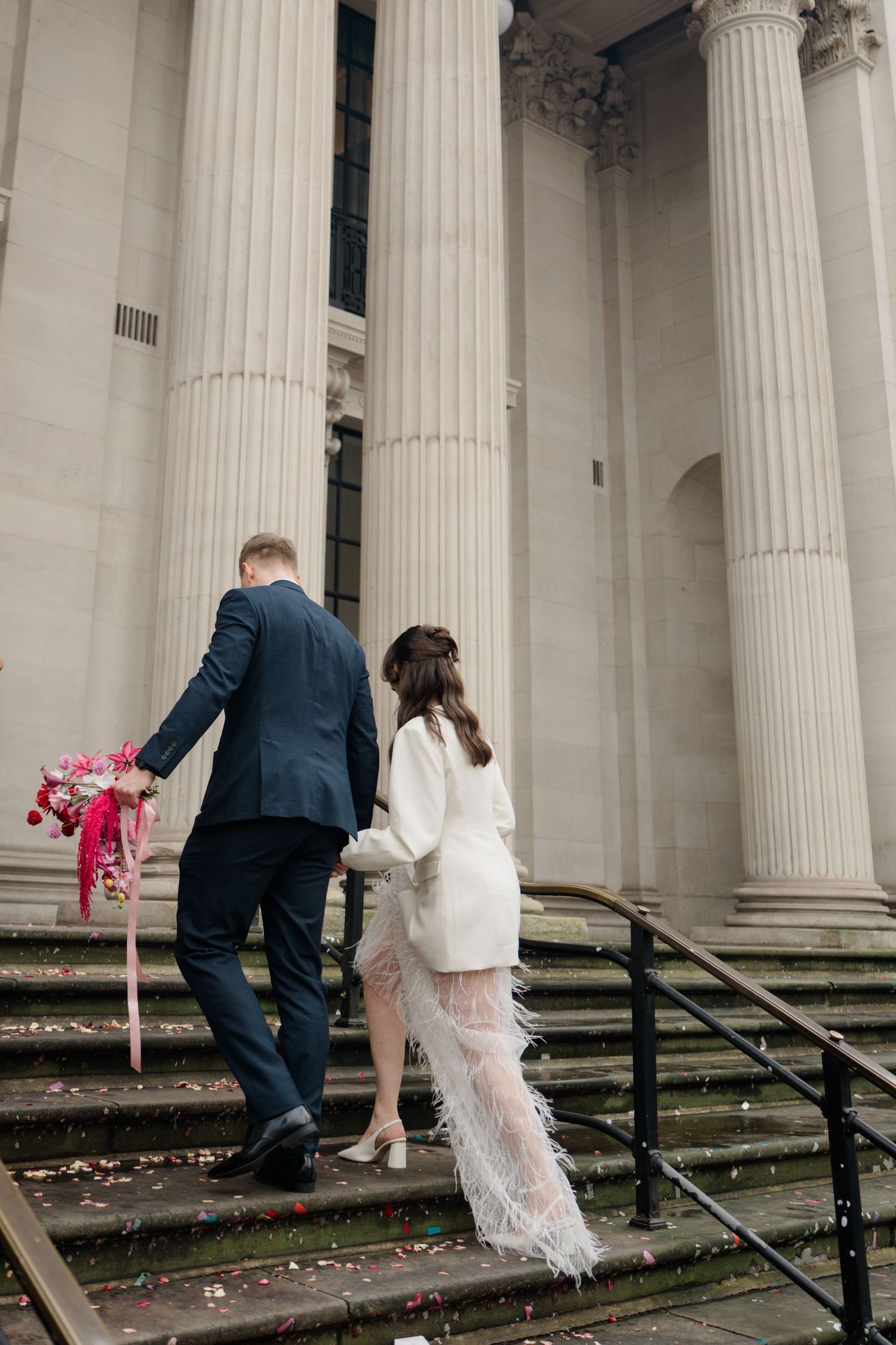 Bride and groom ascending steps of a grand columned building on their wedding day.