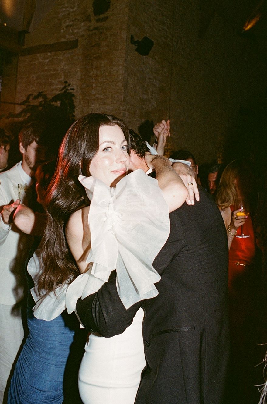 A woman in a white dress hugs a man in a black suit while dancing at an elegant party venue.
