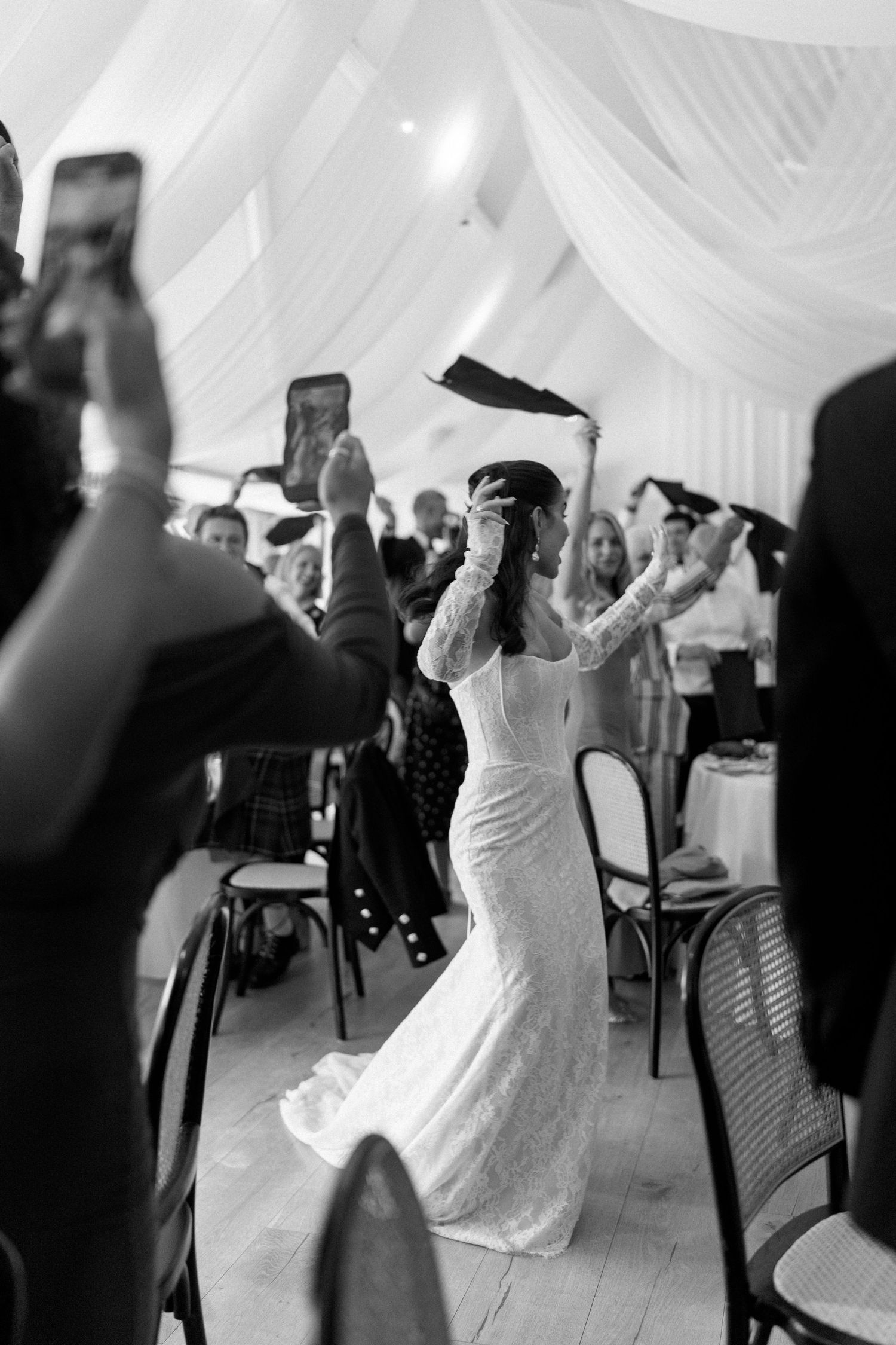 Bride dances energetically through wedding reception hall while guests cheer and film.