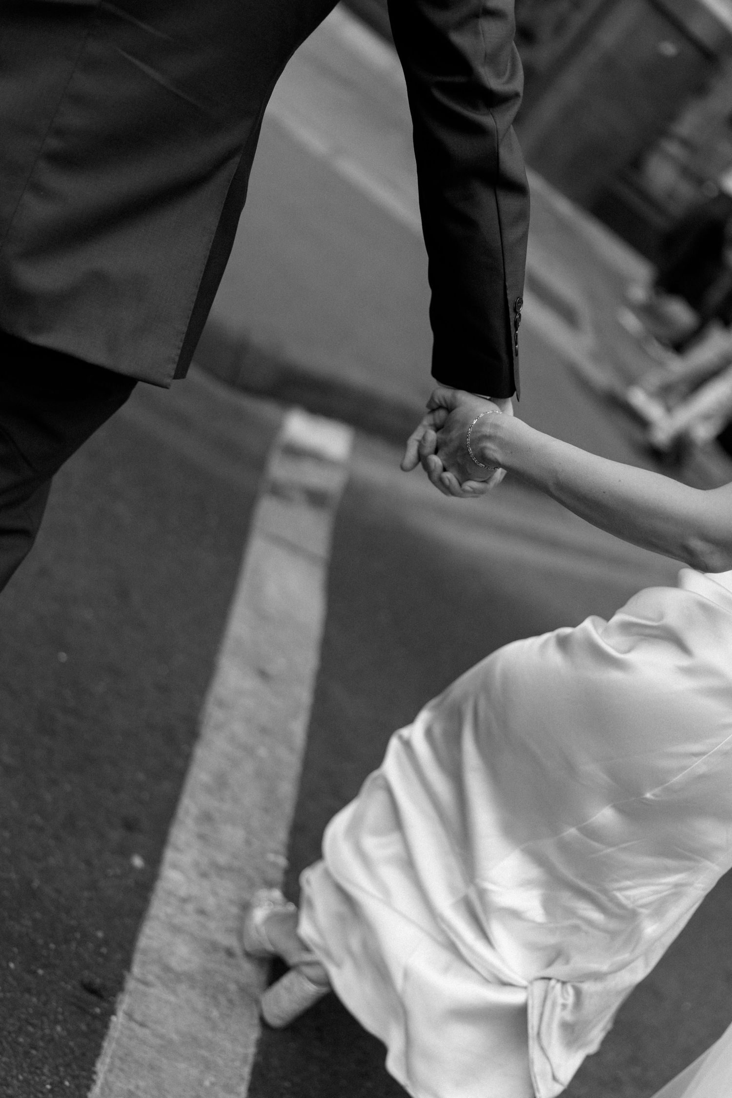 Black and white photo of bride and groom holding hands crossing a city street.