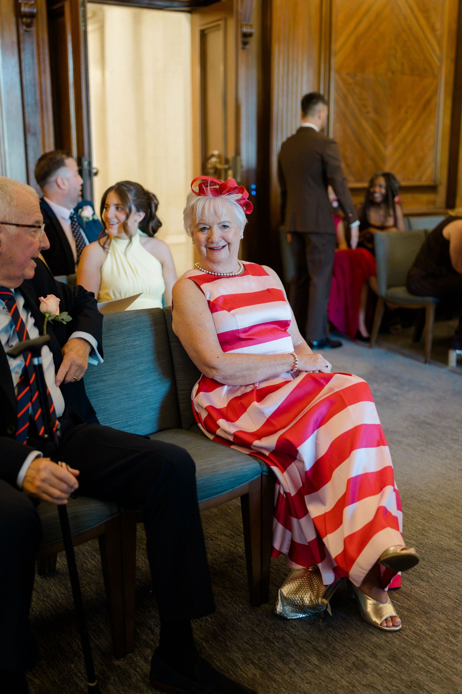 A woman in a bold red and white striped dress sits smiling at an elegant wedding ceremony venue.