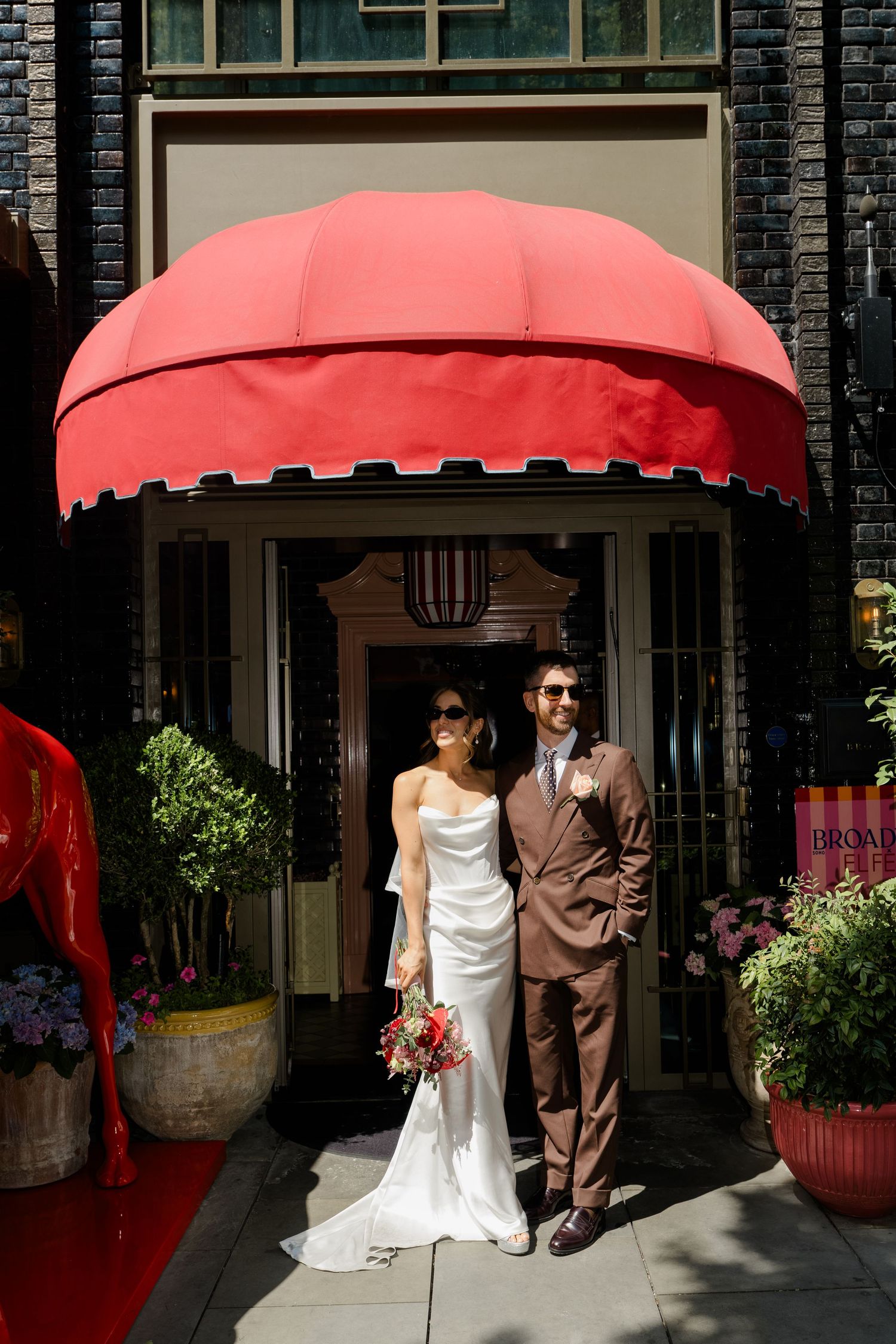 Bride and groom stand beneath a red dome awning at a London venue on their wedding day.